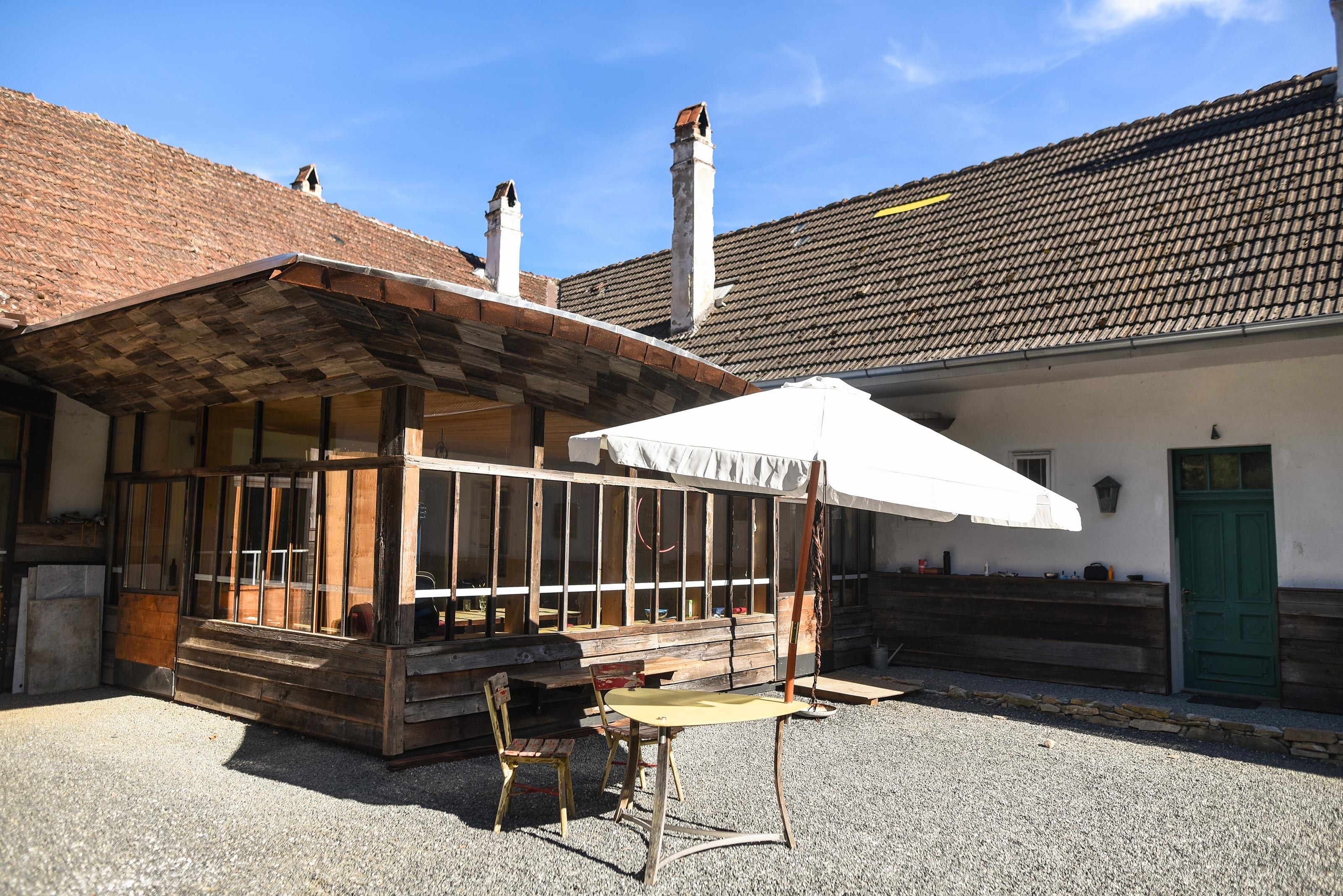 Ein rustikaler Innenhof mit Holzanbau, Tisch und Stühlen unter einem Sonnenschirm.