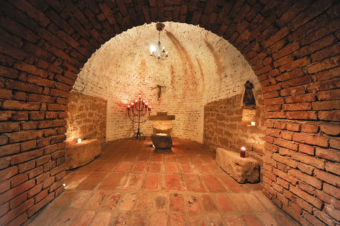 Ein rustikaler, gewölbter Kellerraum mit Kerzen und einem Altar.