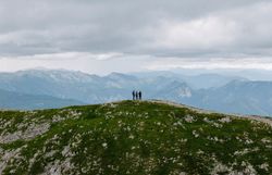 Drei wandernde Personen stehen auf einem Wanderweg entlang eines Kamms, dahinter die Berglandschaft.