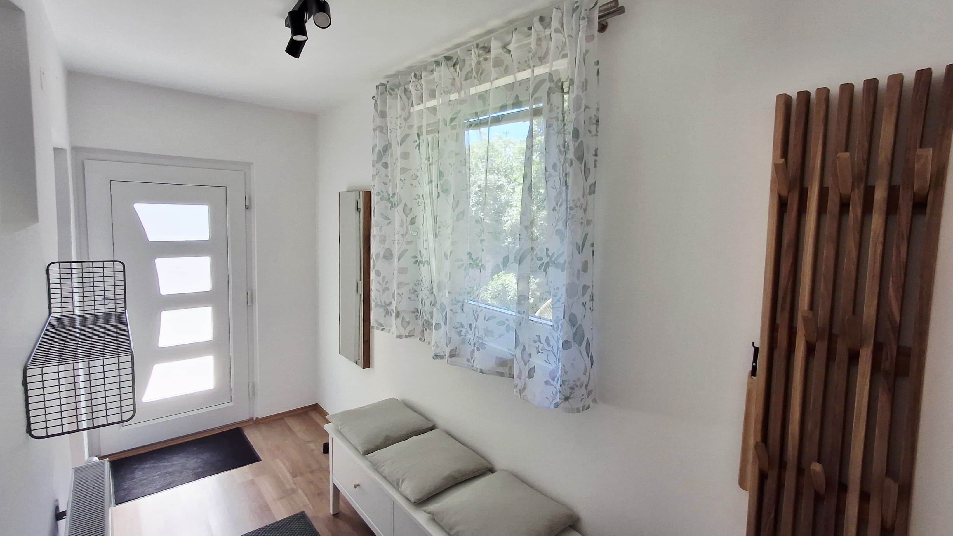 Heller Eingangsbereich mit weißer Tür, Holzfußboden, Sitzbank und Garderobe.