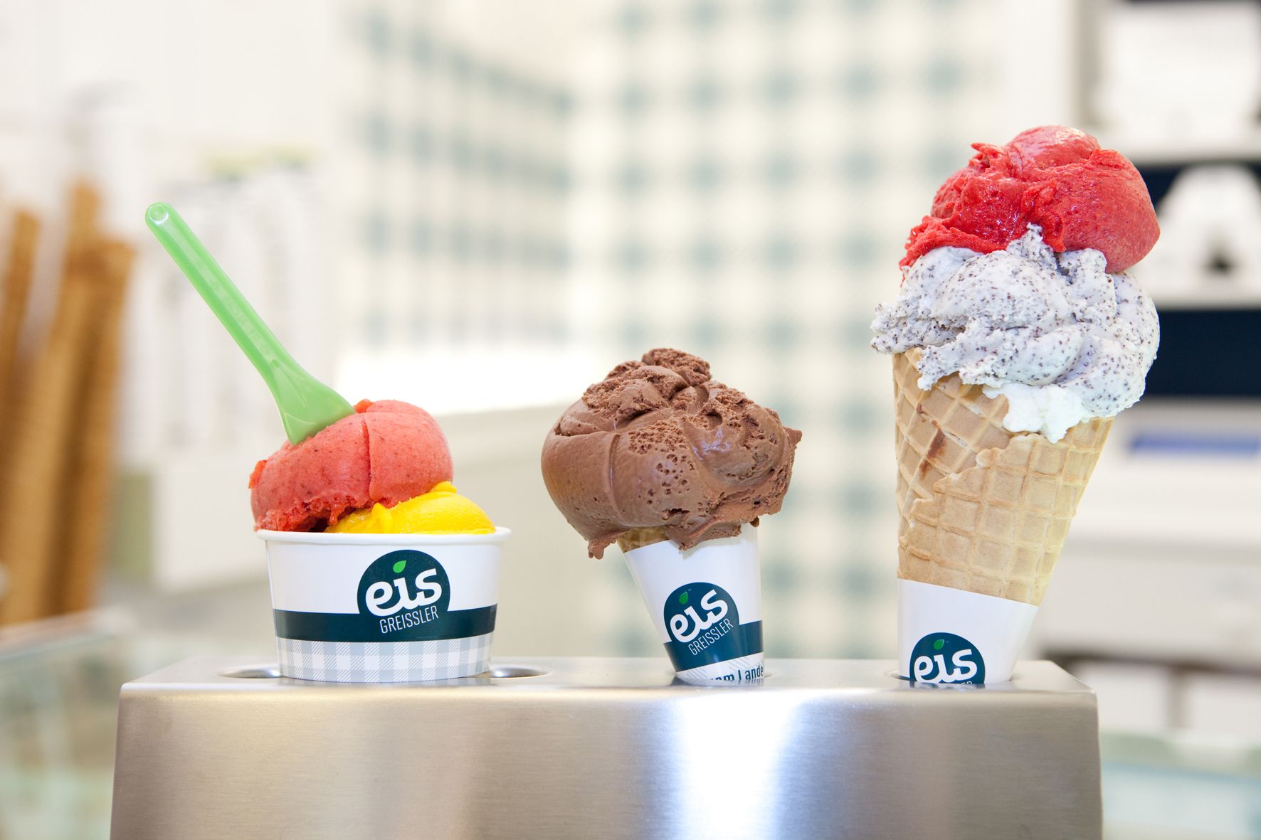 Drei Eissorten von Eis Greissler in Bechern und Waffel.