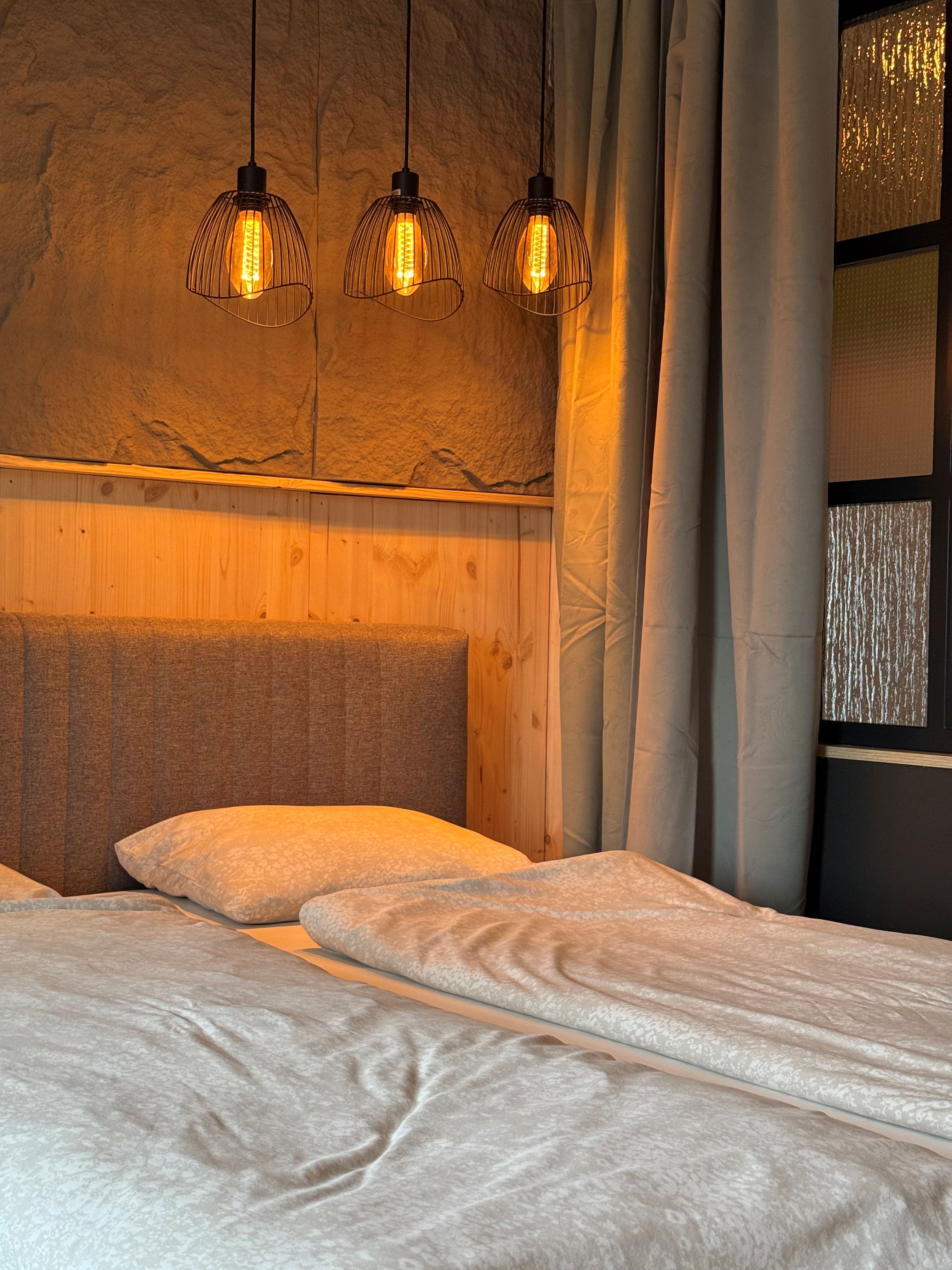 Gemütliches Schlafzimmer mit Doppelbett, Holzverkleidung und drei hängenden Lampen.