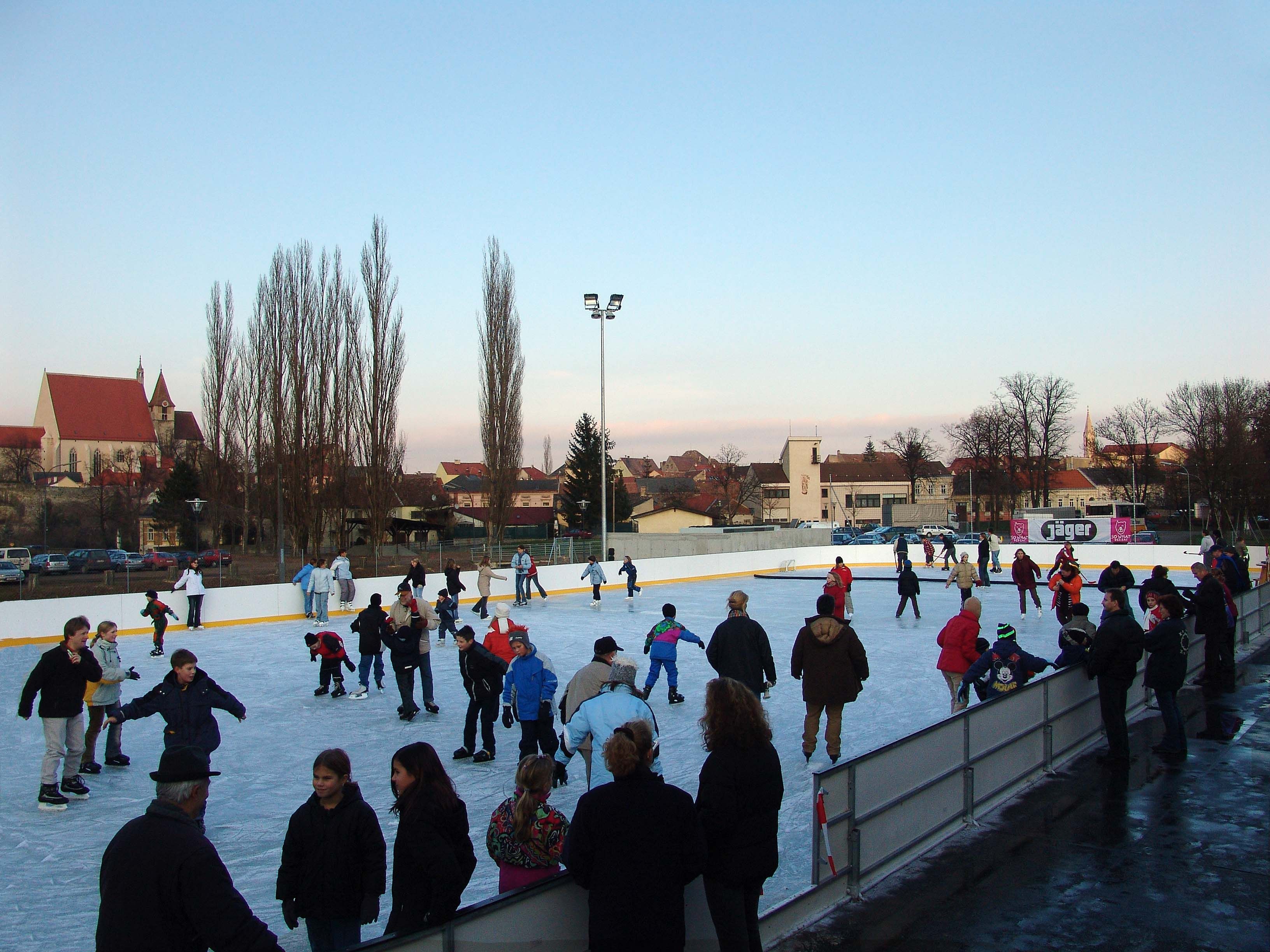 Menschen beim Eislaufen auf einem Freiluft-Eislaufplatz mit einer Kirche im Hintergrund.