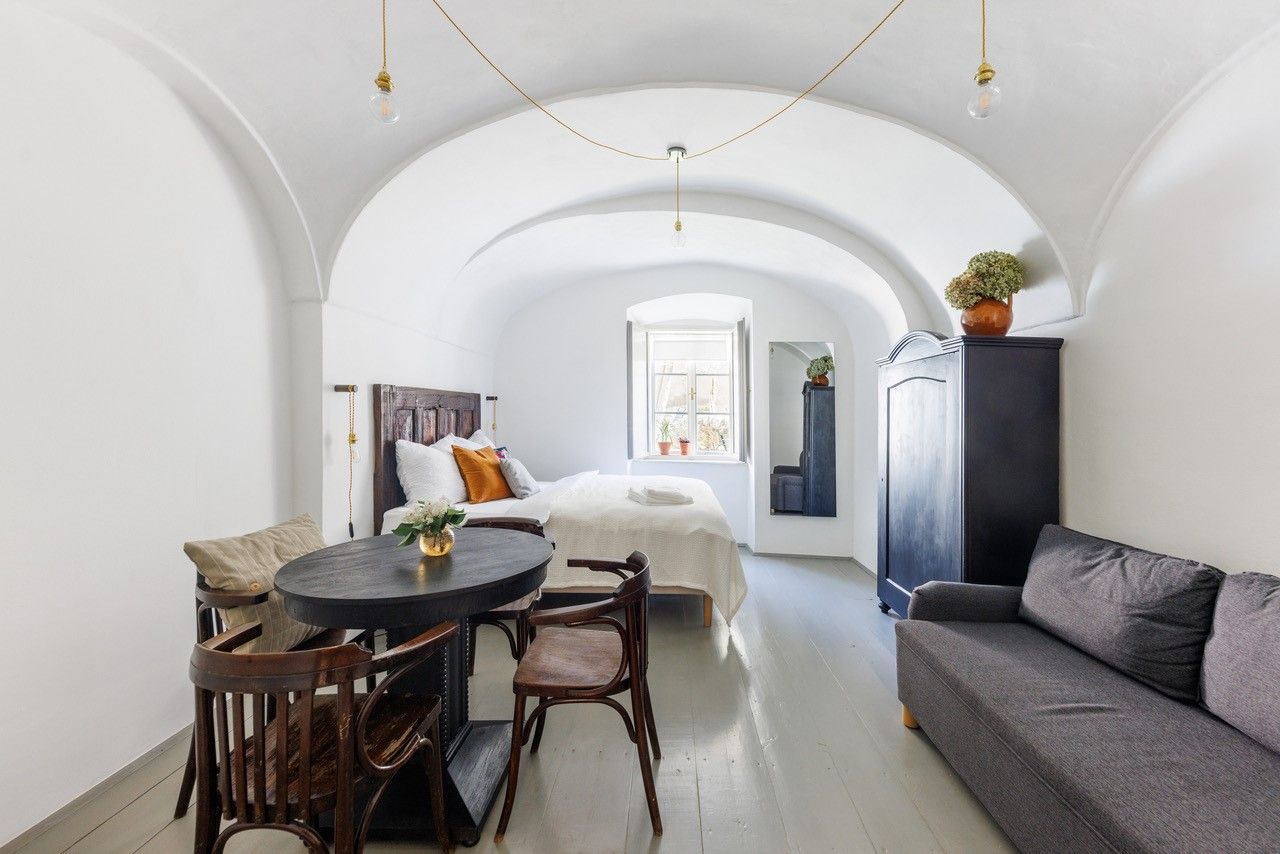 Ein stilvoll eingerichtetes Gästezimmer mit gewölbter Decke, Bett, Sofa, Tisch und Stühlen. Ein Fenster lässt Tageslicht herein.