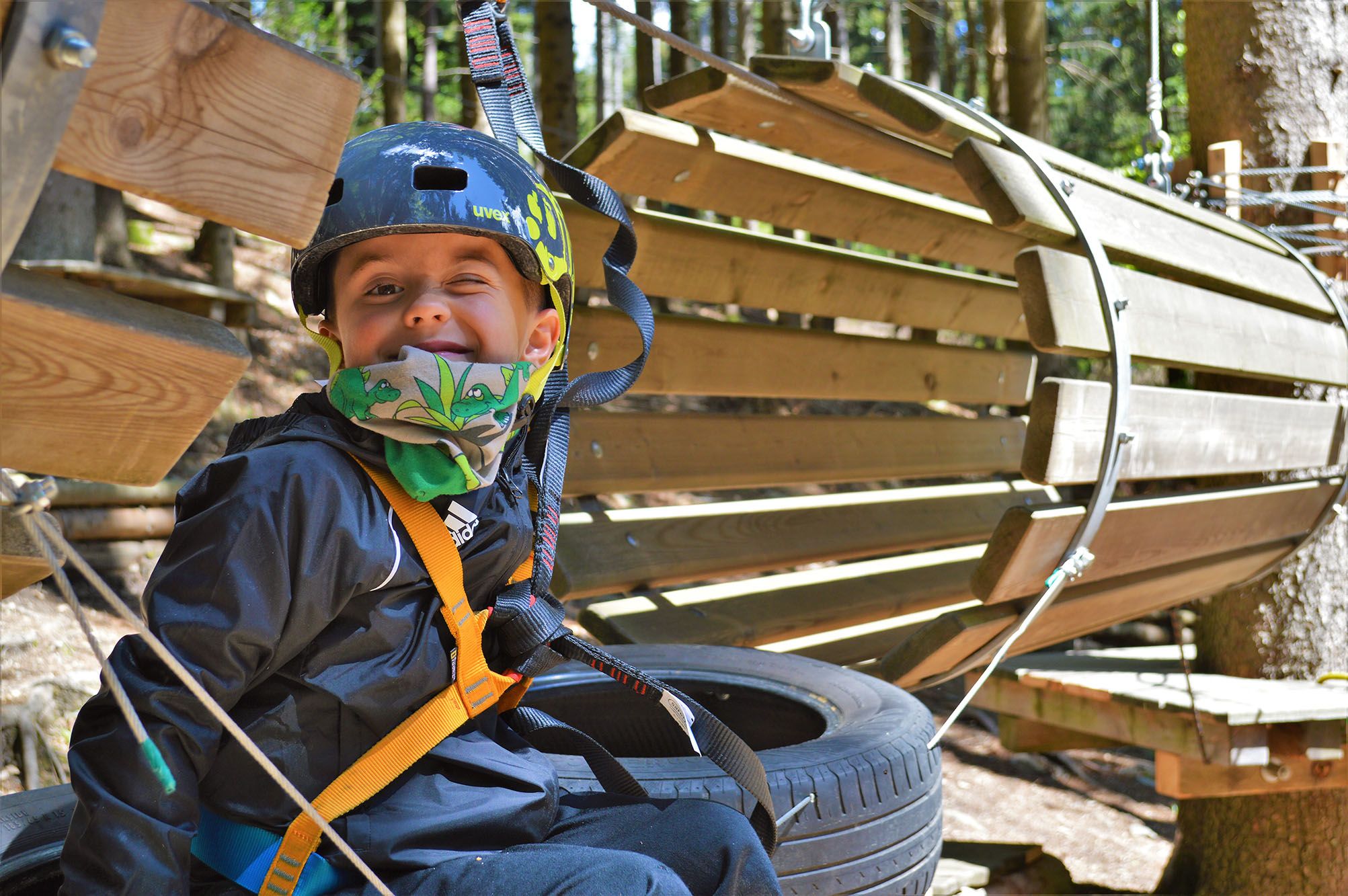Ein Kind mit Helm und Sicherheitsgurt in einem Kletterpark.