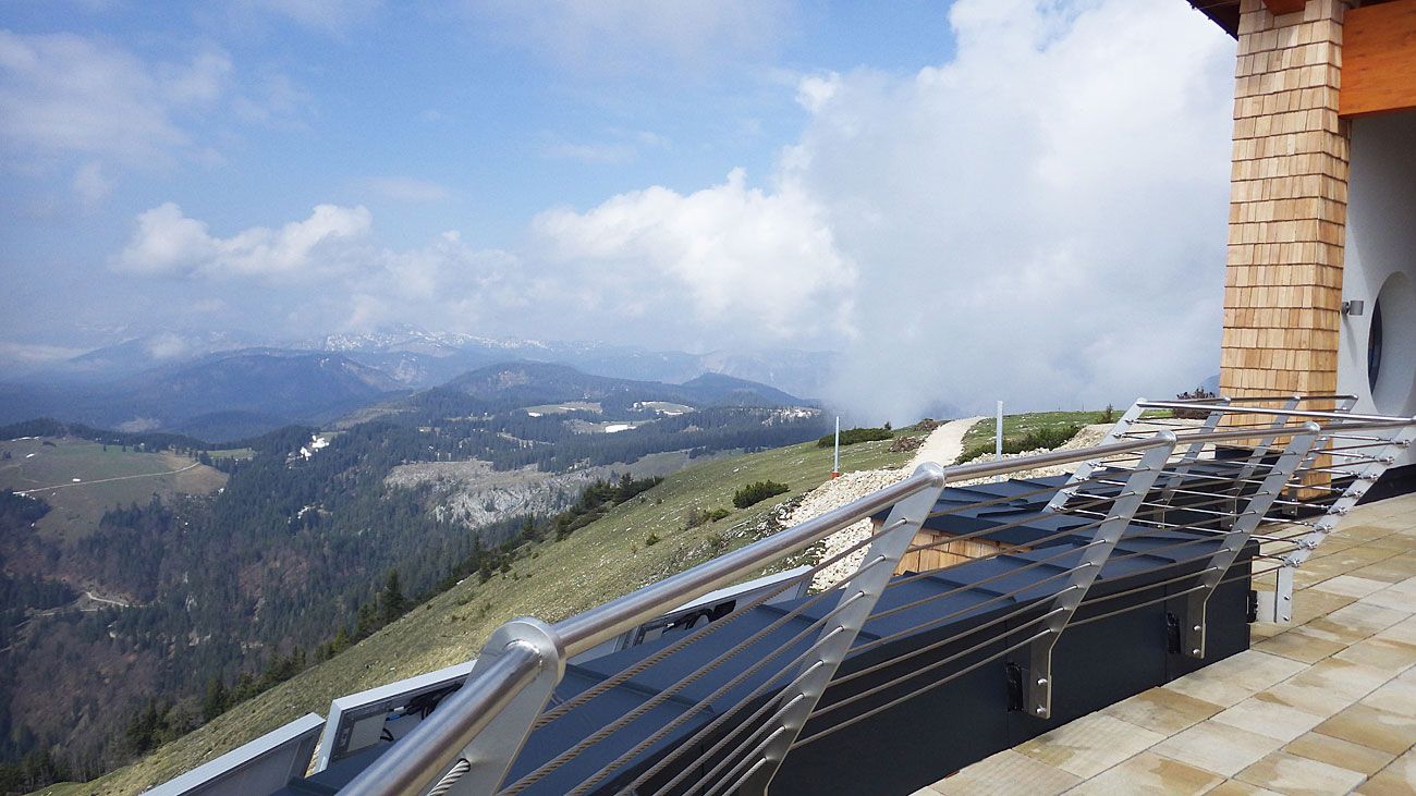 Aussicht vom Terzerhaus auf eine bergige Landschaft mit Wolken und einem Geländer im Vordergrund.