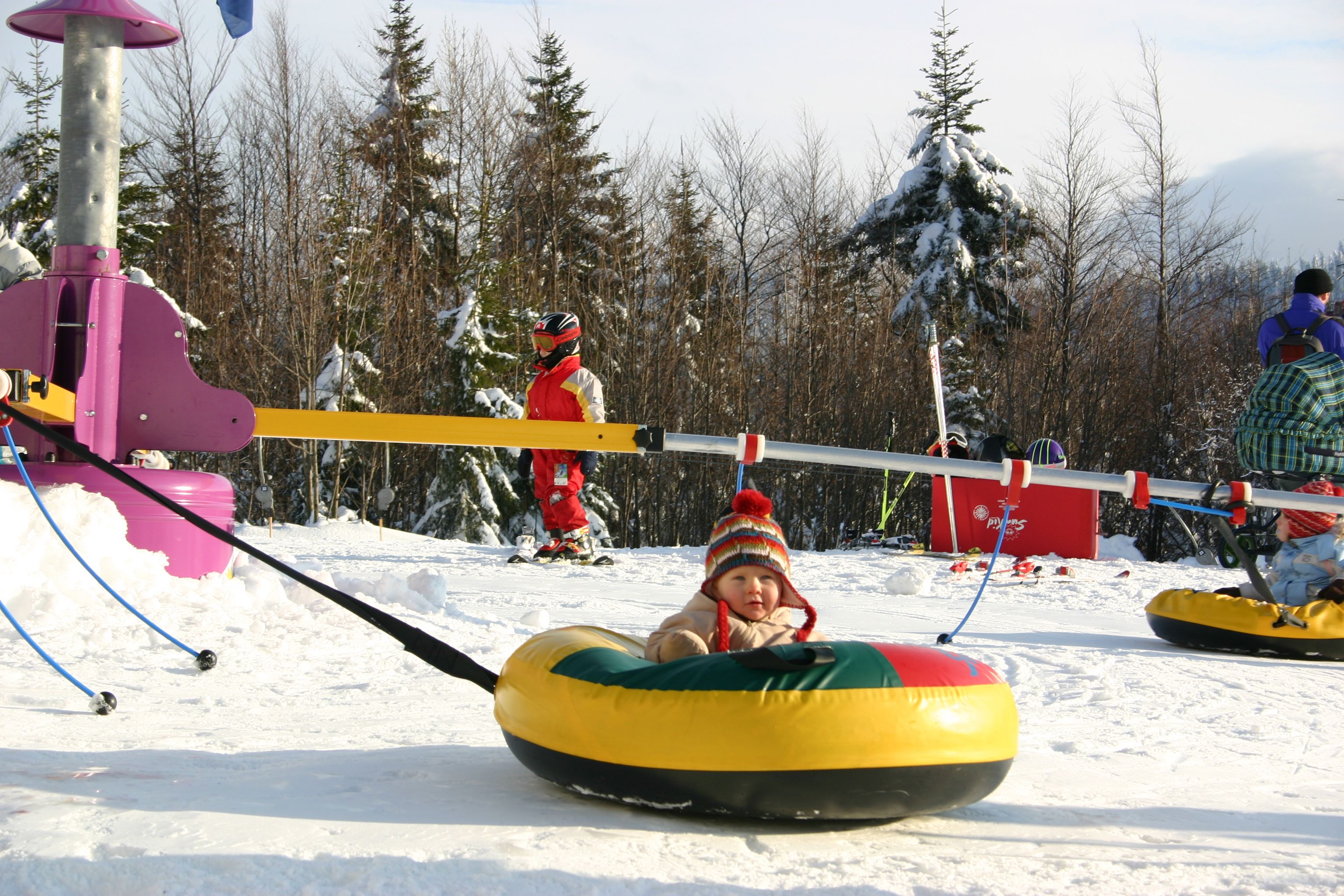 Kinder im Schneepark mit Tubingreifen und Skiausrüstung.