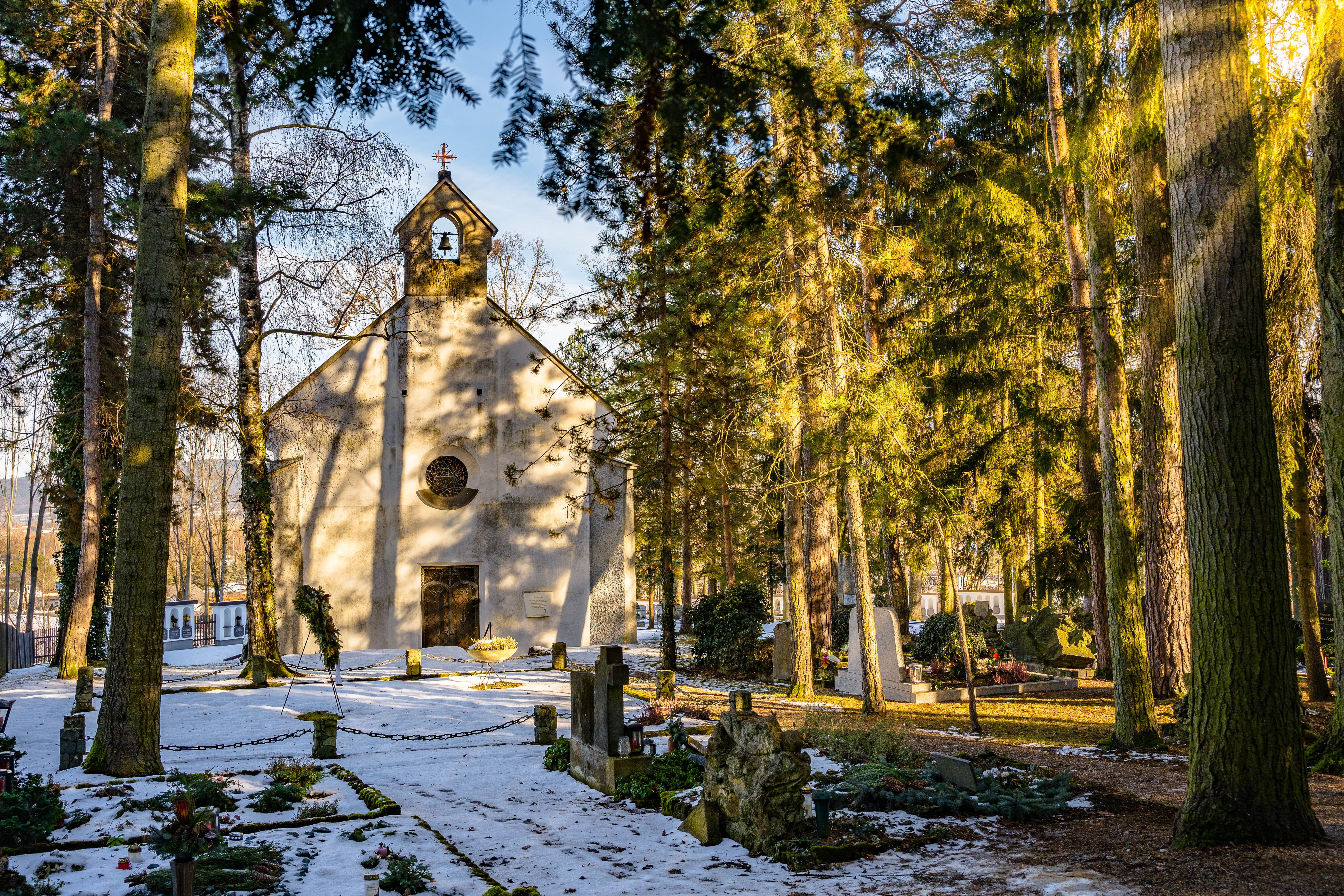 Winterliche Kapelle im Wald mit schneebedecktem Boden und Gräbern.