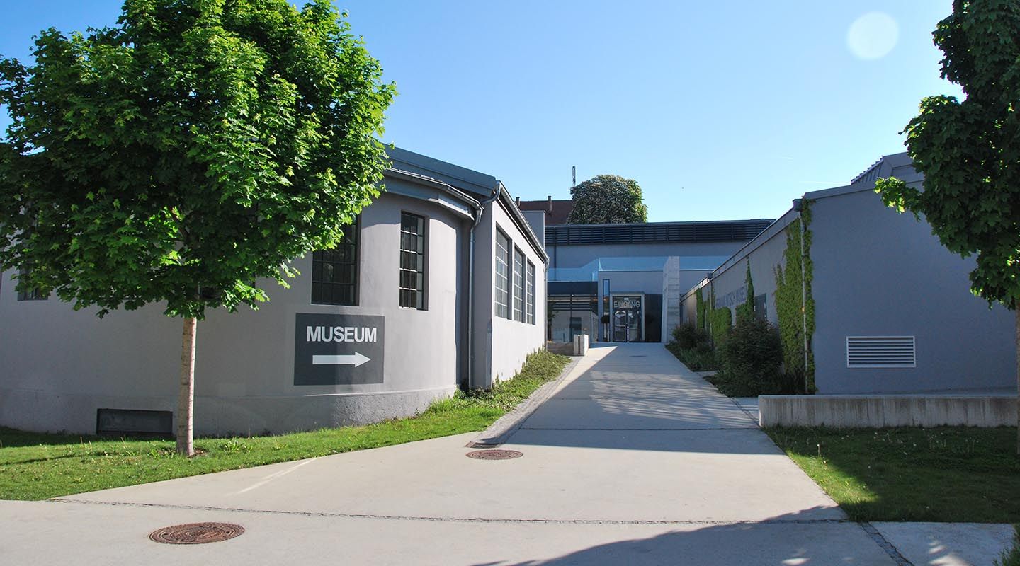Eingang des MAMUZ Museums Mistelbach mit Wegweiser und Bäumen.