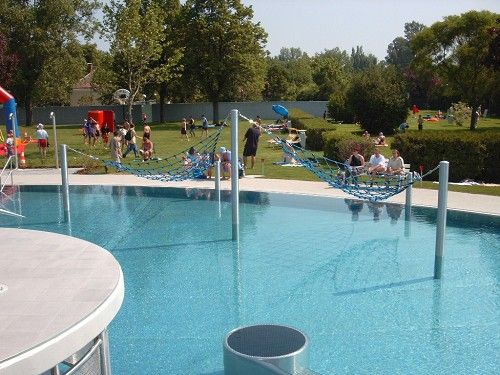 Ein Freibad mit Hängematten über dem Wasser und Menschen im Hintergrund auf der Liegewiese.
