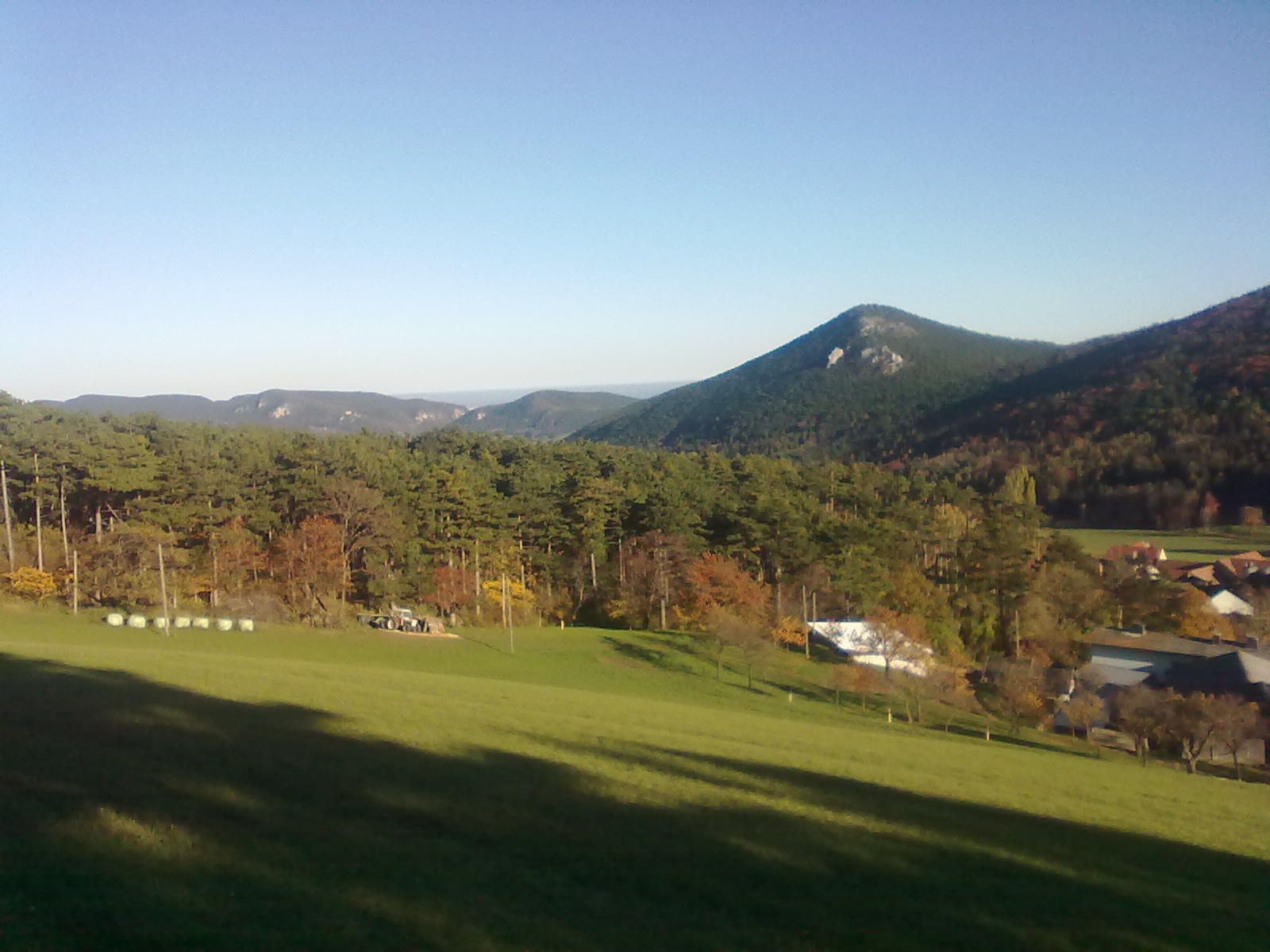 Landschaft mit Hügeln, Wald und Wiesen unter klarem Himmel.