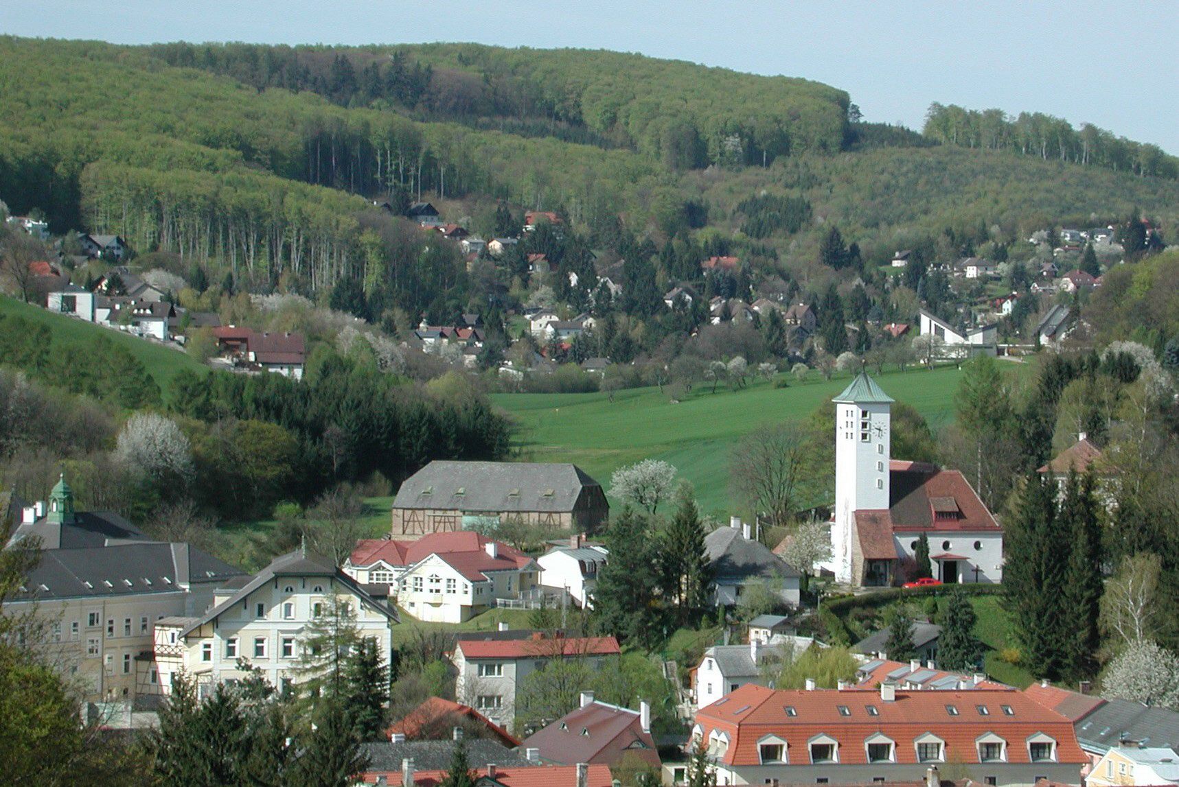 Panorama von Gablitz mit Kirche und umliegenden Häusern vor bewaldeten Hügeln.