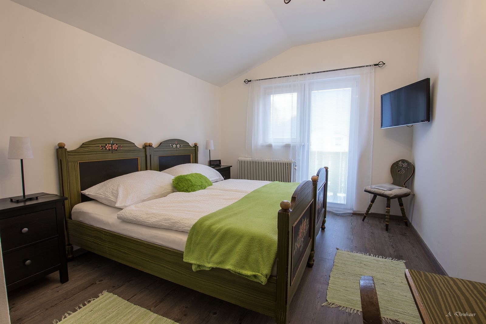 Gemütliches Schlafzimmer mit Doppelbett, grüner Bettdecke und TV an der Wand.