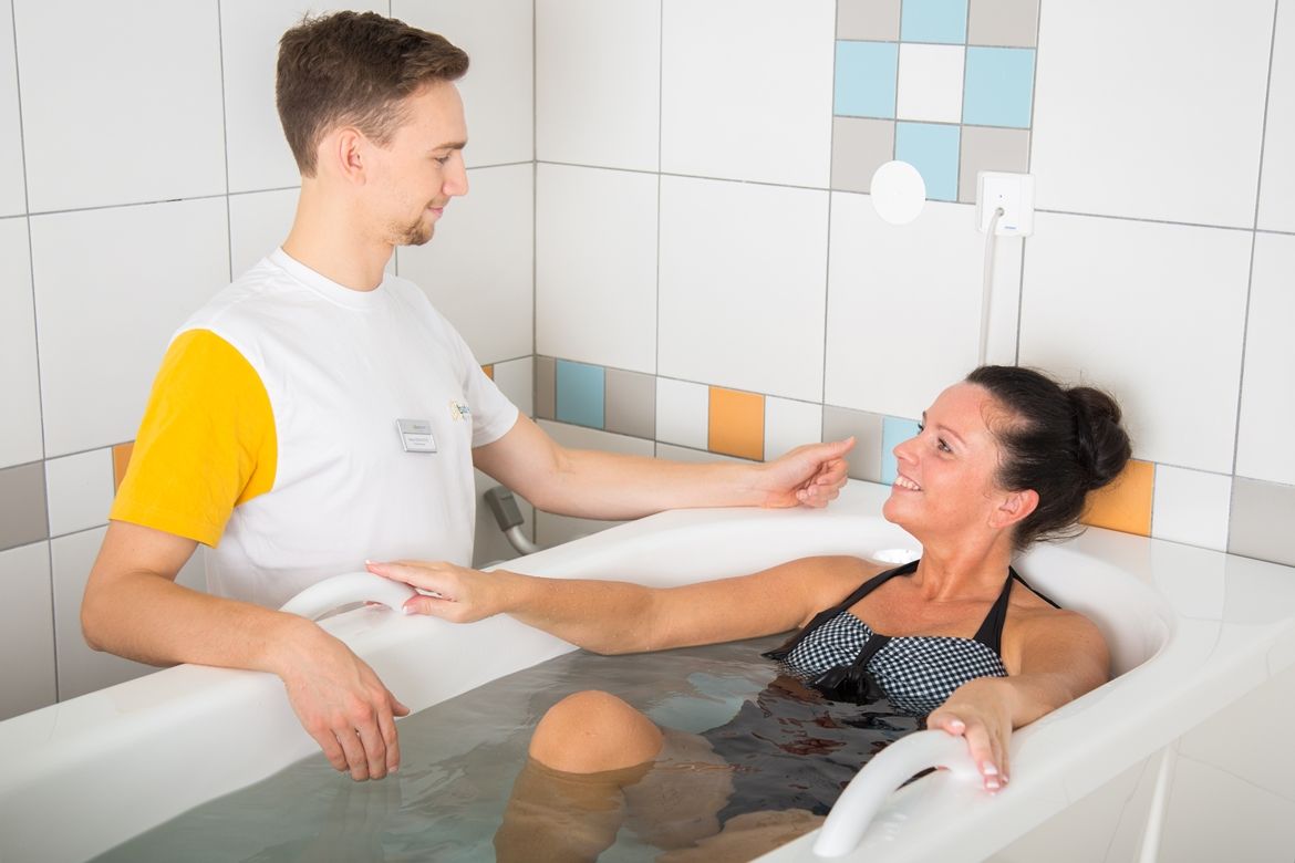 Eine Frau in einem Schwefelbad wird von einem Therapeuten betreut.