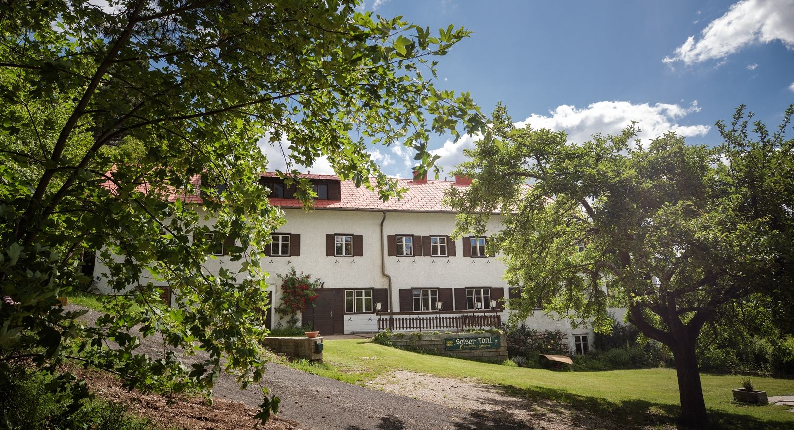 Ein traditionelles Gebäude mit roten Dachziegeln und weißen Wänden, umgeben von grünen Bäumen und einem blauen Himmel.