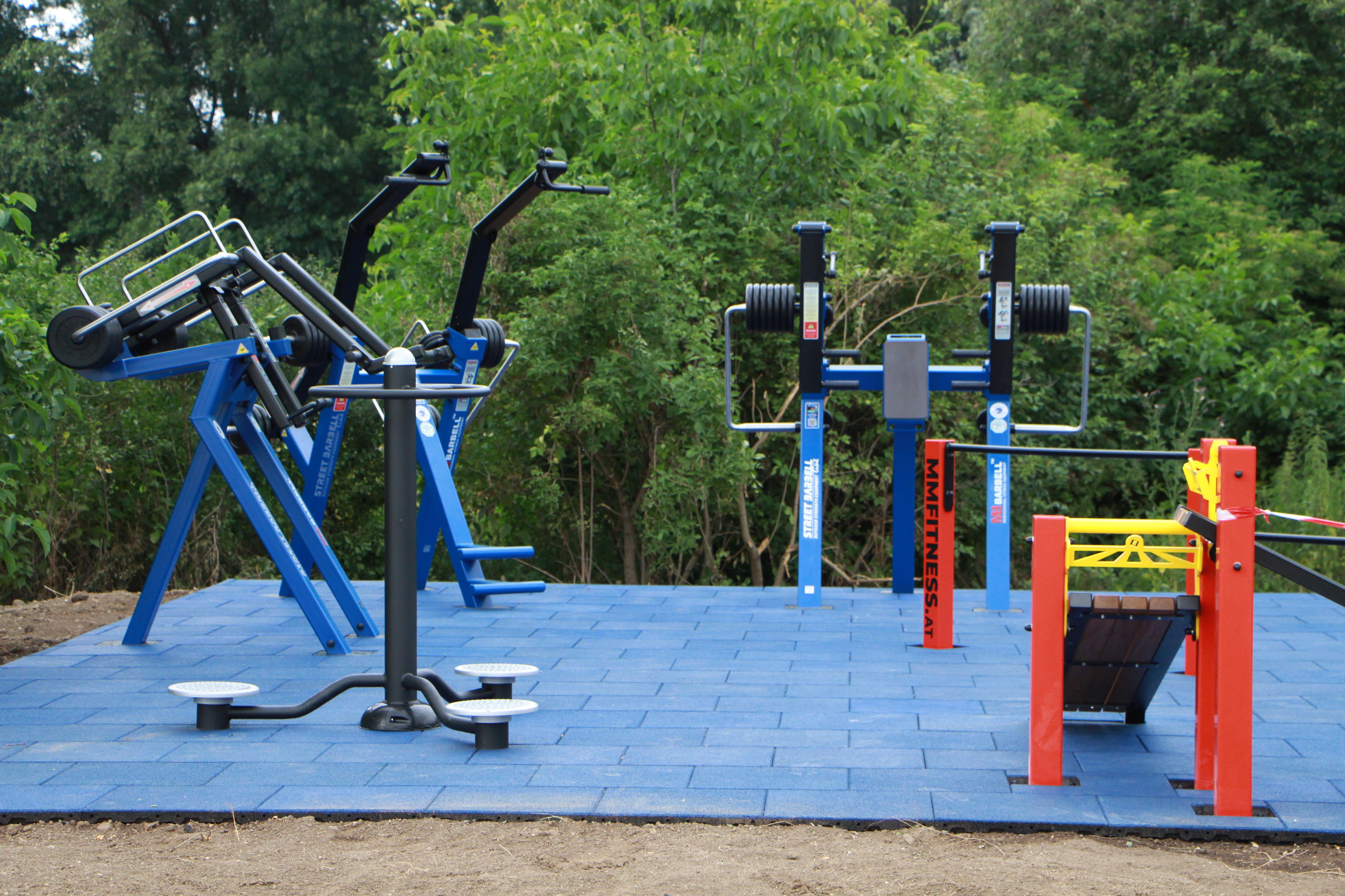 Outdoor-Fitnessgeräte auf blauen Bodenplatten im Freien.