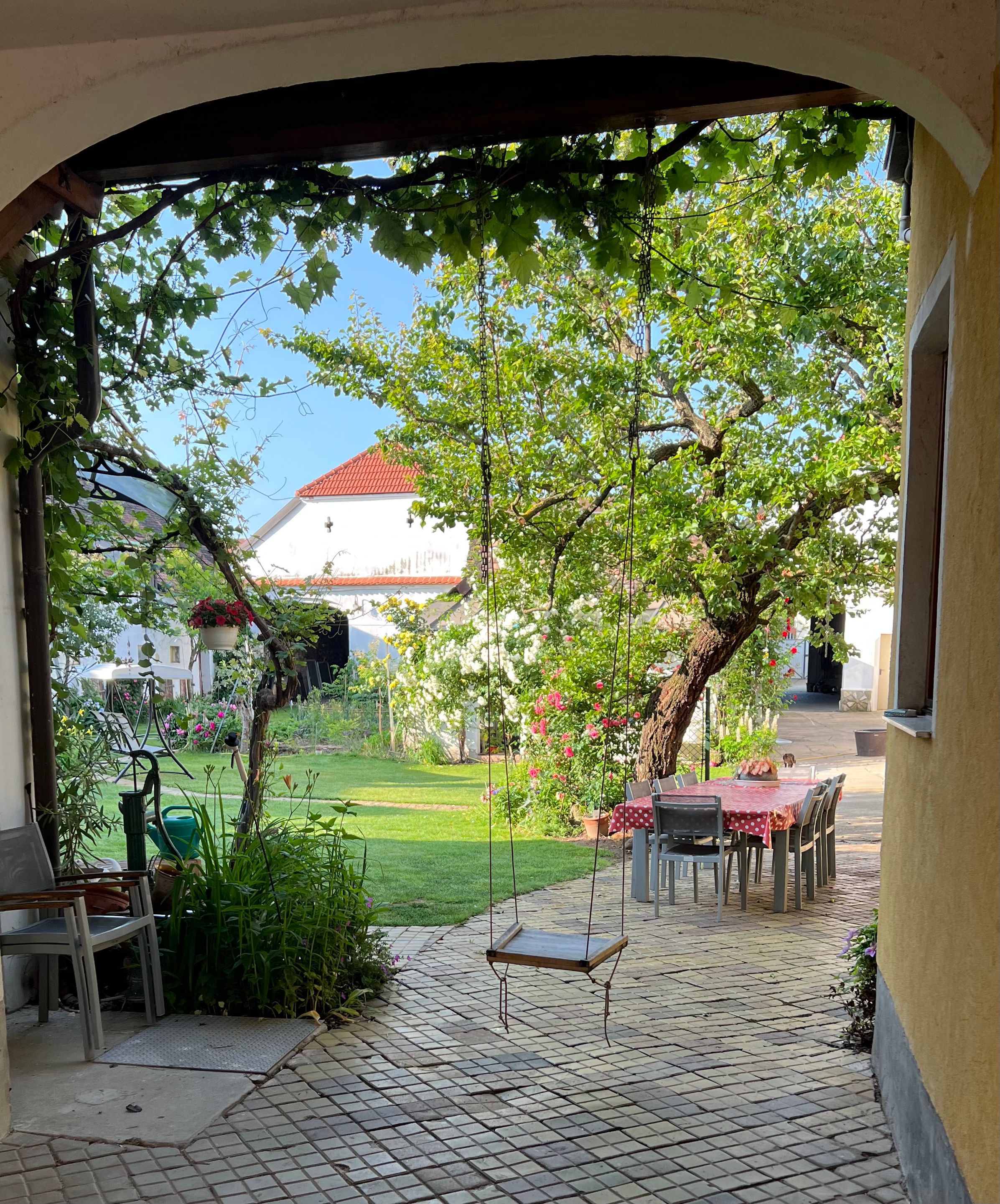 Ein idyllischer Garten mit einer Schaukel, einem Tisch mit Stühlen und blühenden Pflanzen.