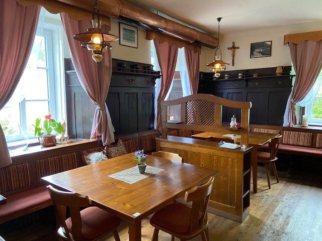 Gemütliche Gaststube mit Holzmöbeln und rosa Vorhängen.