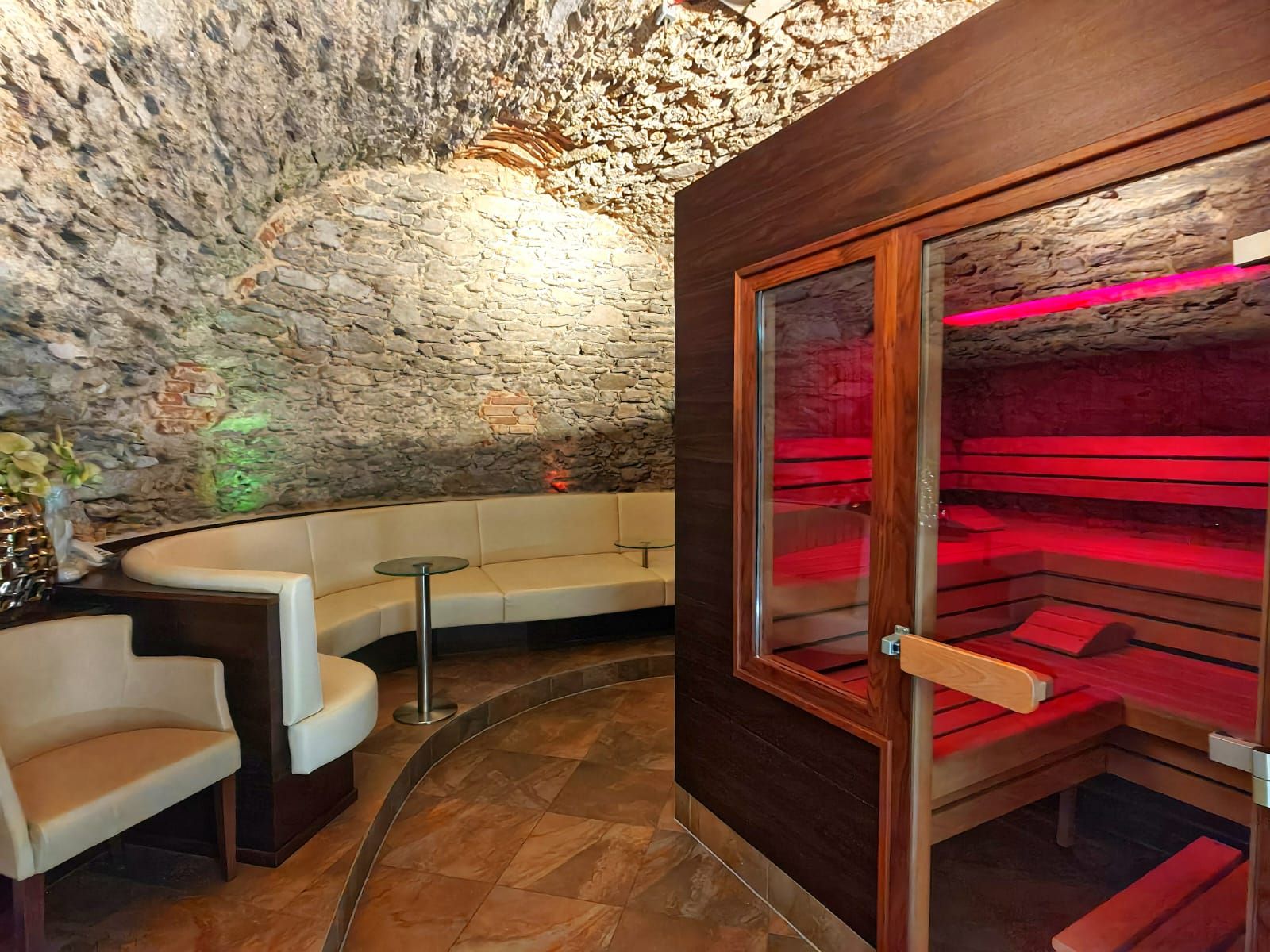 Ein gemütlicher Wellnessbereich mit einer Sauna und einer Sitzgruppe in einem Raum mit gewölbter Steinwand.