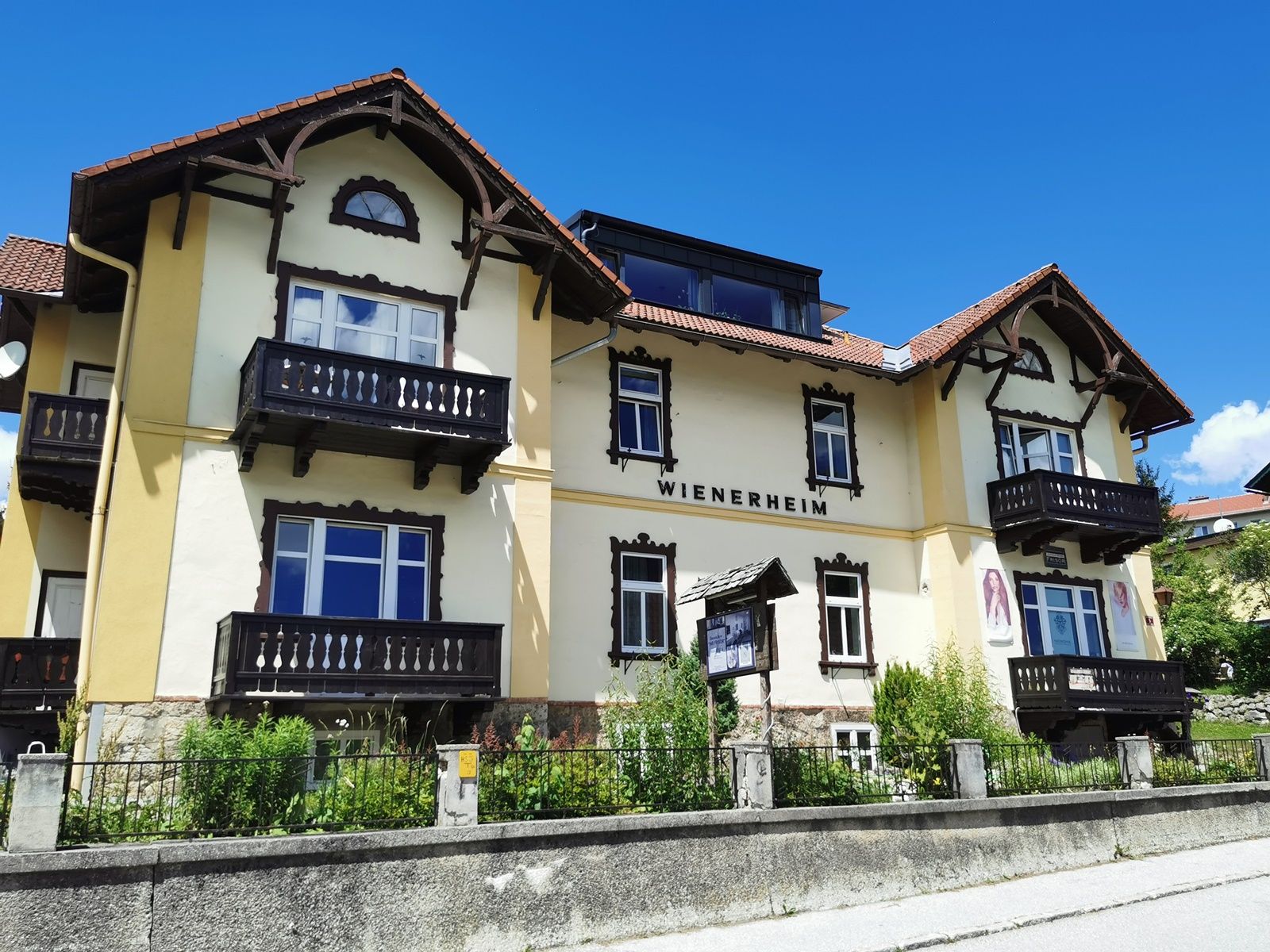 Gelbes Gebäude mit der Aufschrift 'WIENERHEIM', Holzbalkone und blauer Himmel.
