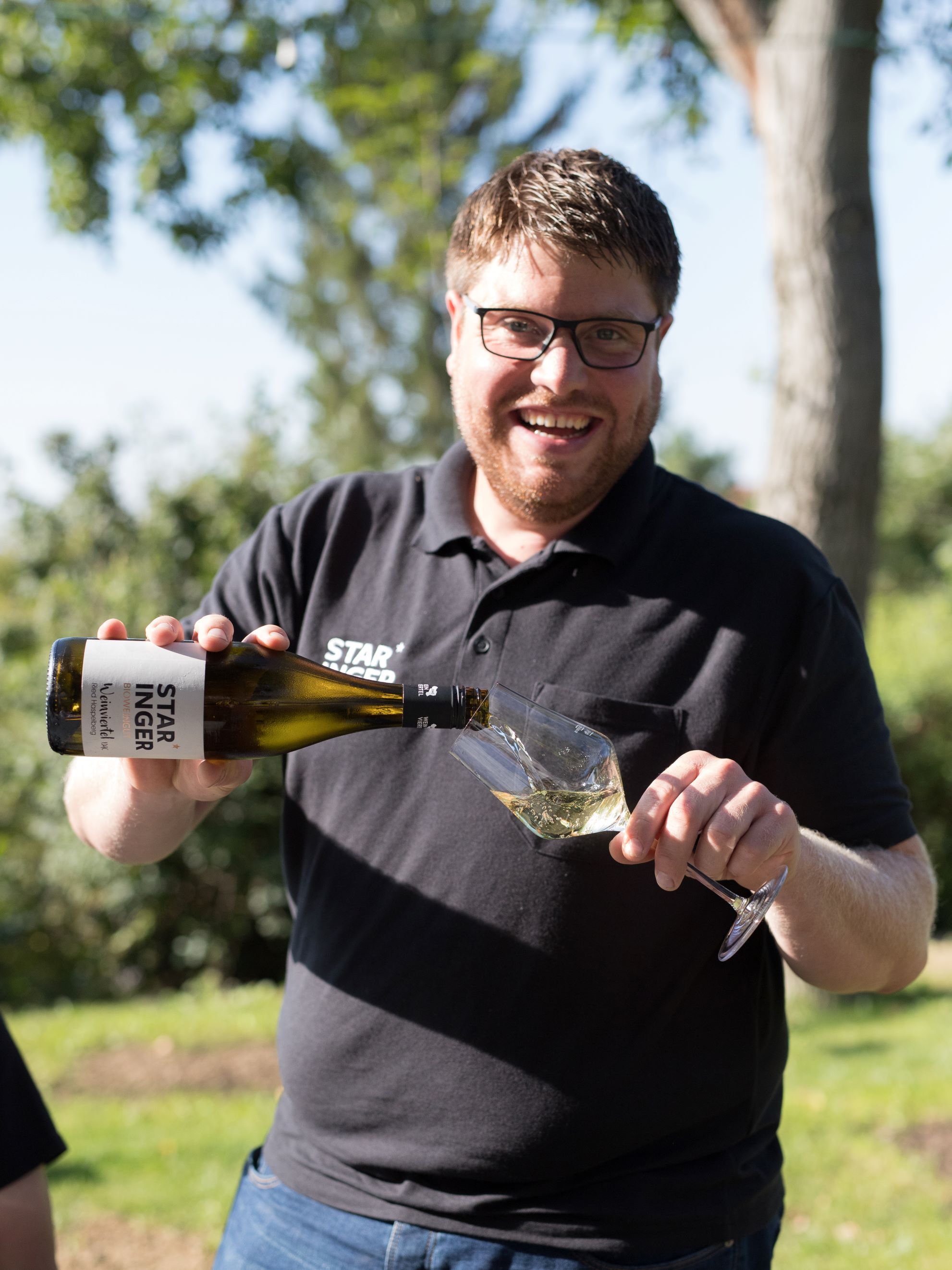 Mann schenkt Wein in ein Glas im Freien ein.