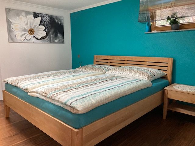 Schlafzimmer mit Doppelbett, türkisfarbener Wand und Blumenbild.