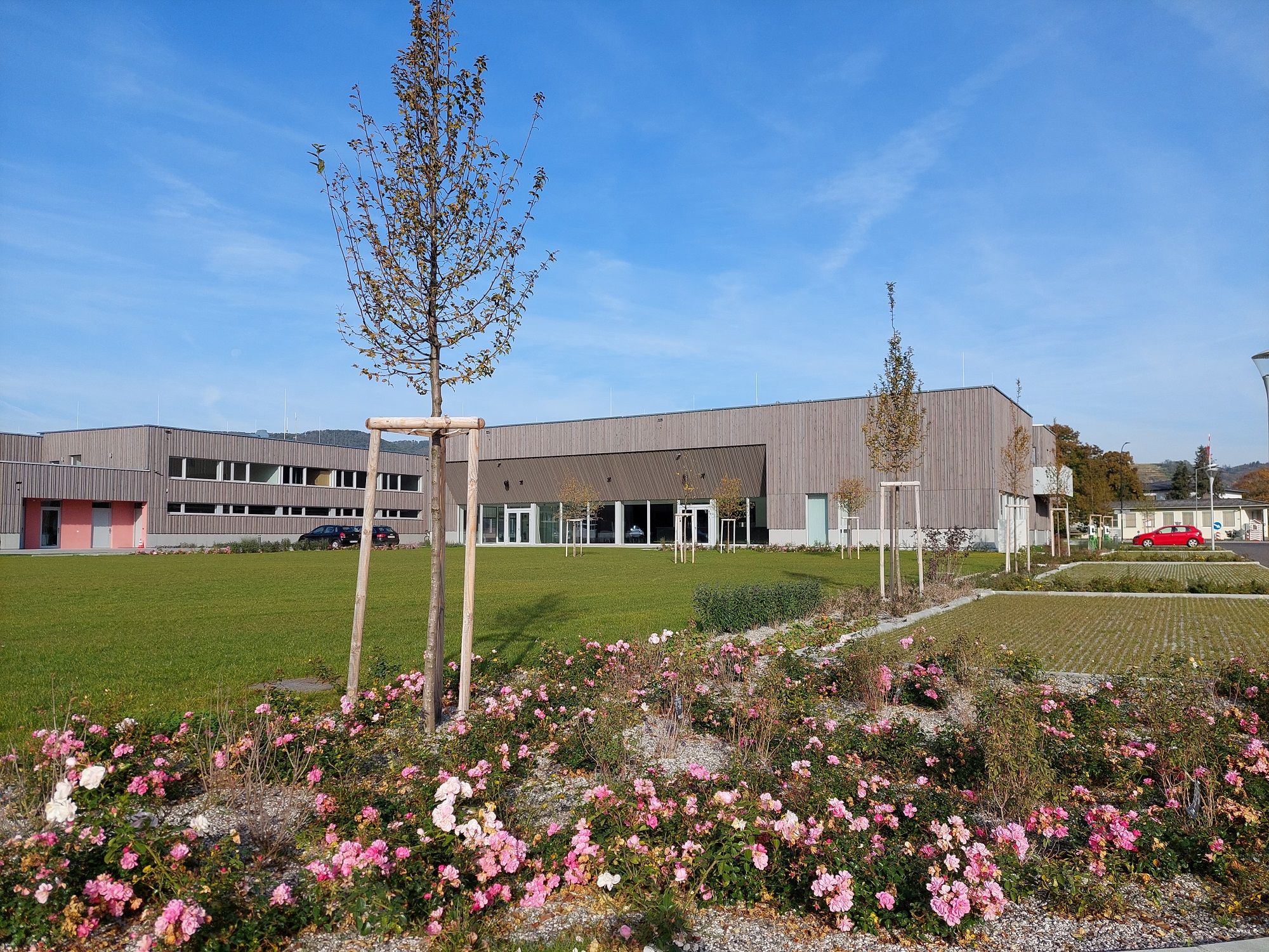 Moderne Gebäude mit Holzfassade und gepflegter Gartenanlage im Vordergrund.