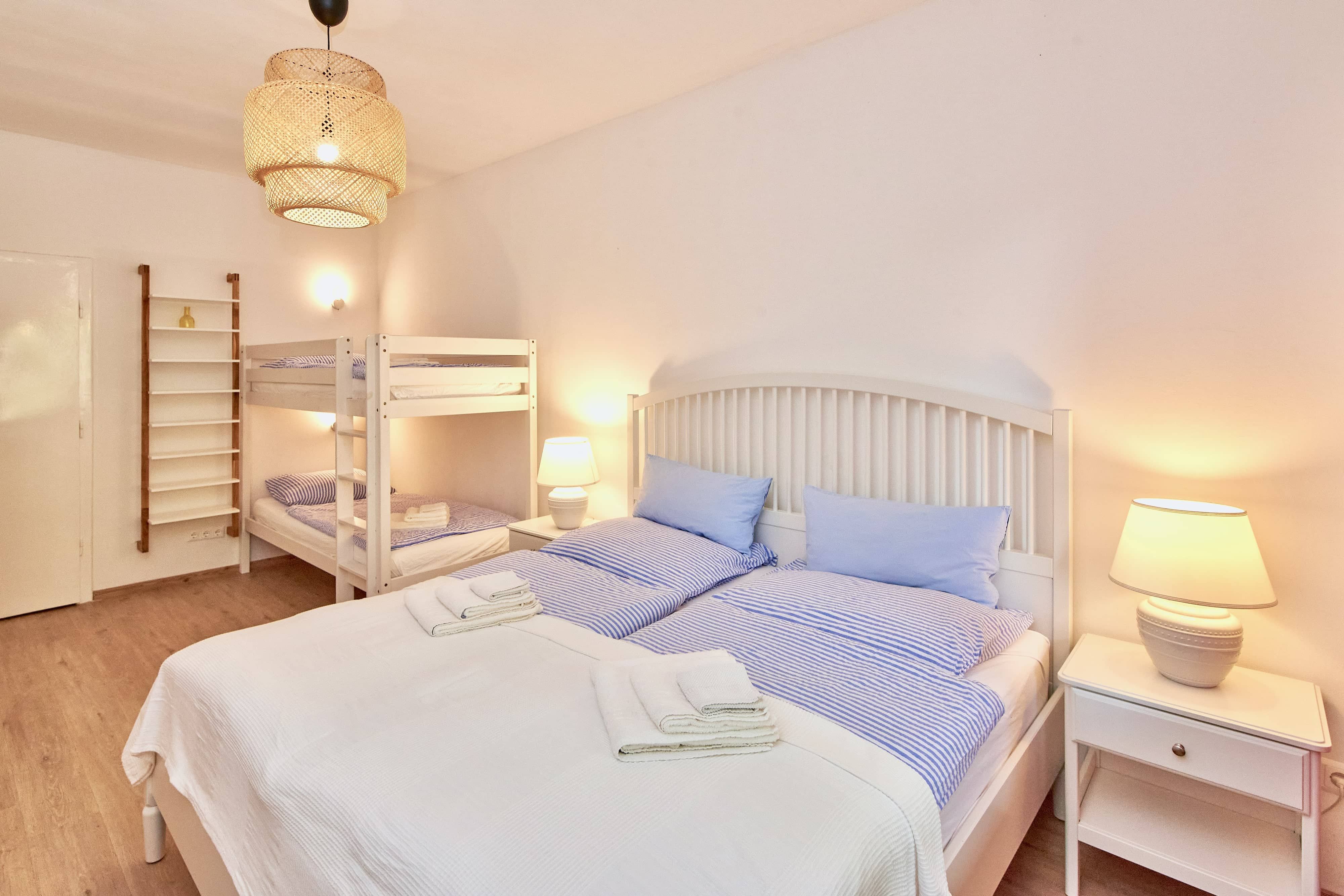 Schlafzimmer mit Doppelbett, Etagenbett, Nachttischlampen und heller Einrichtung.