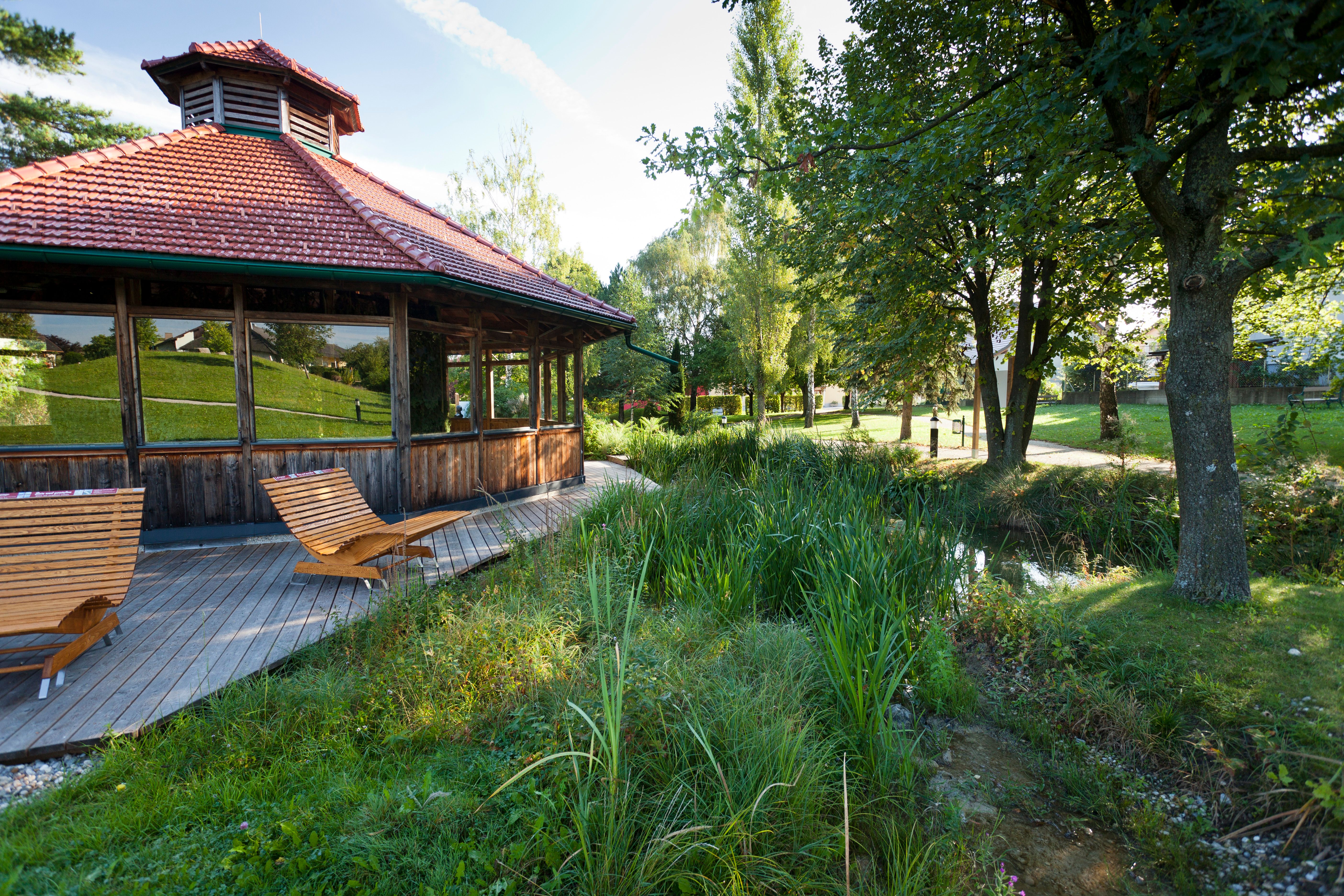 Holzpavillon mit Liegestühlen in einem grünen Park.