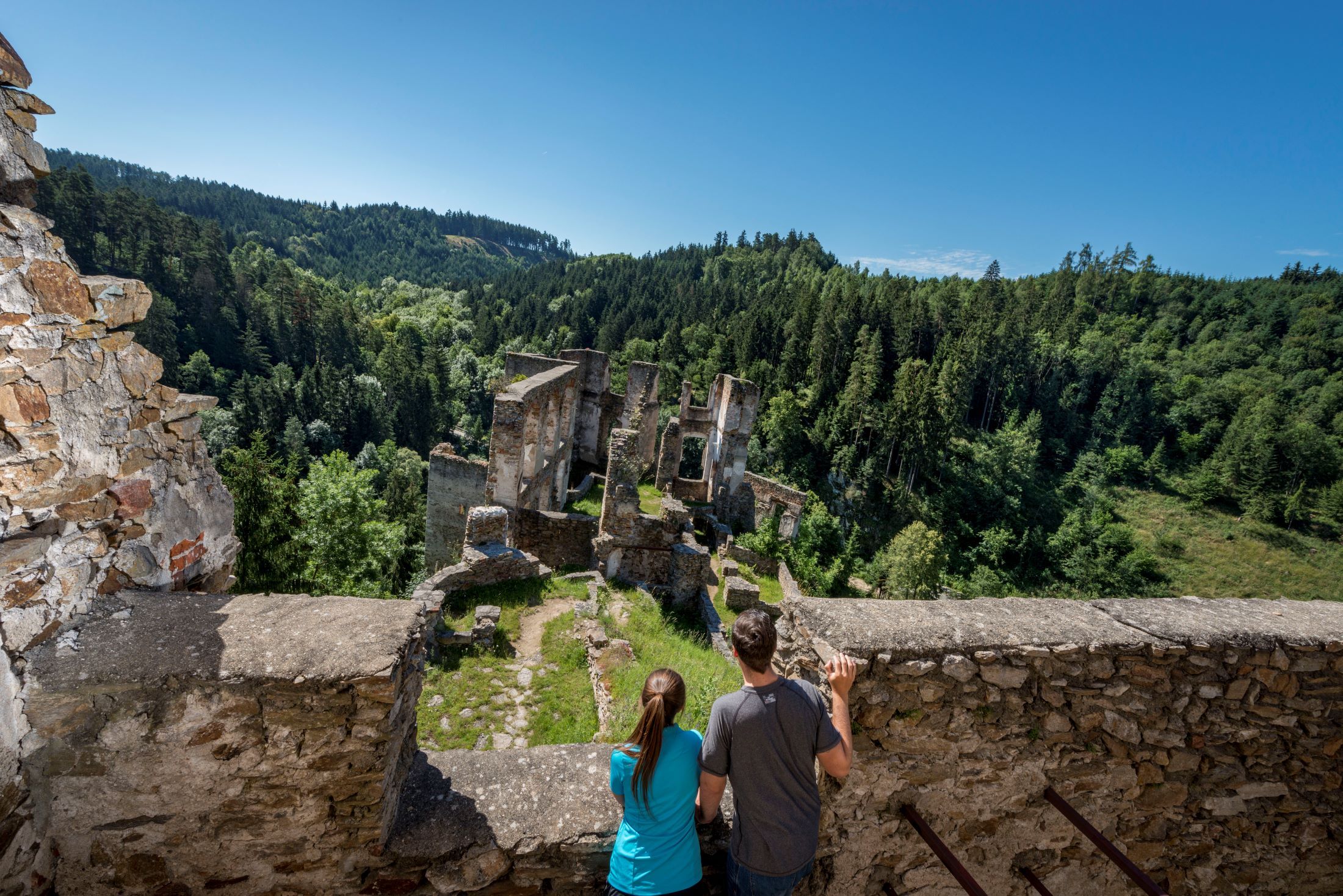 Zwei Personen betrachten die Ruine Kollmitz inmitten eines bewaldeten Tals.