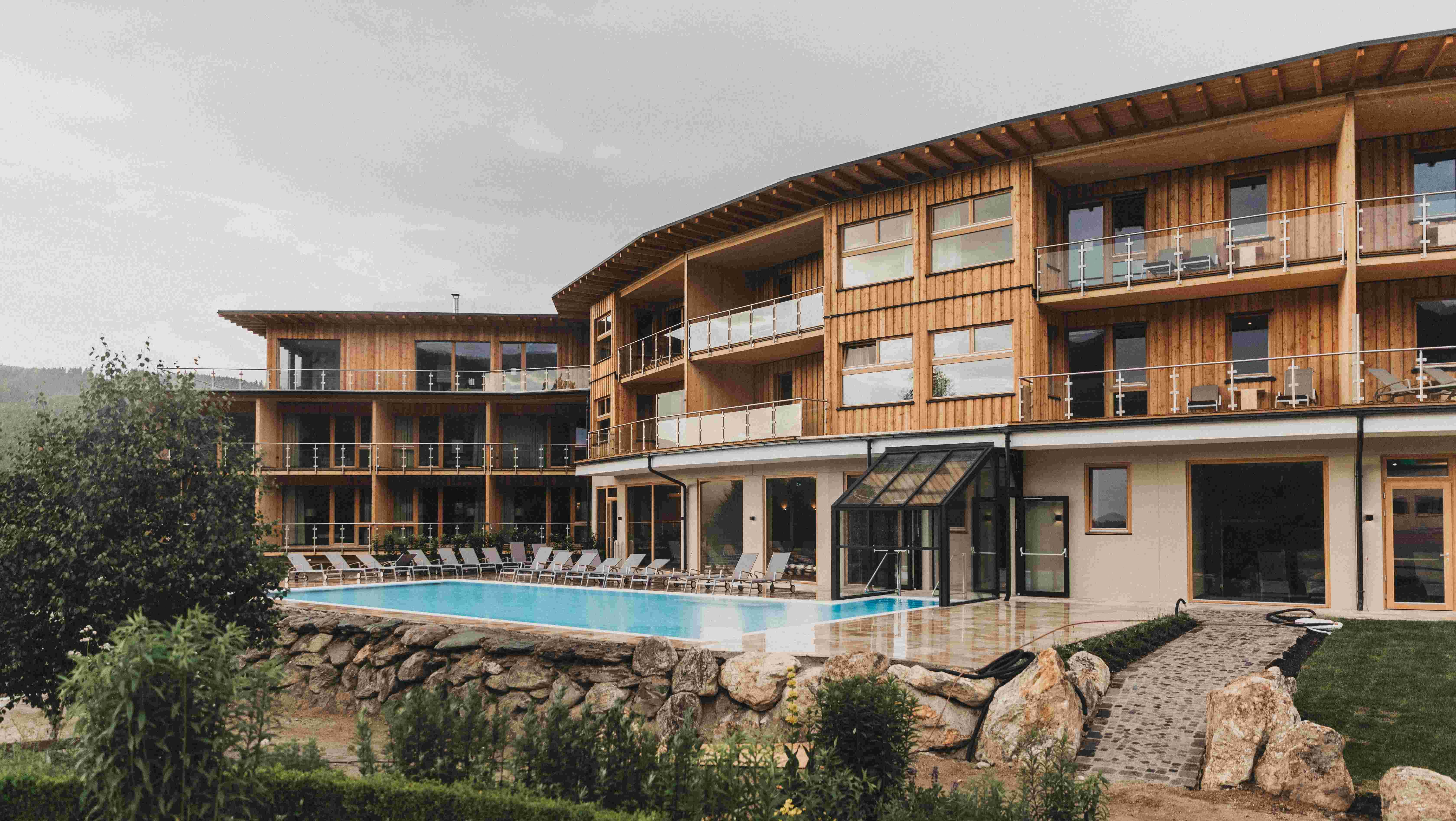 Außenansicht eines modernen Holzgebäudes mit Pool und Liegestühlen.