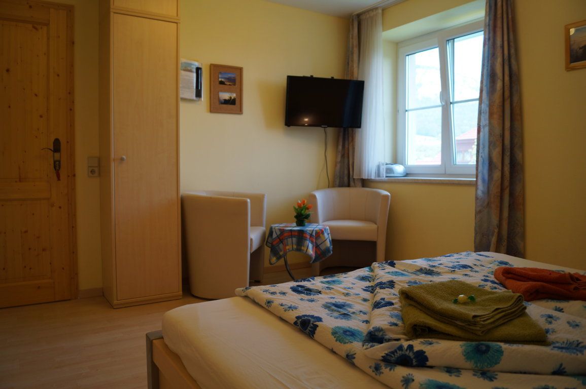 Komfortzimmer mit Bett, zwei Sesseln, Tisch, Fernseher und Fenster.