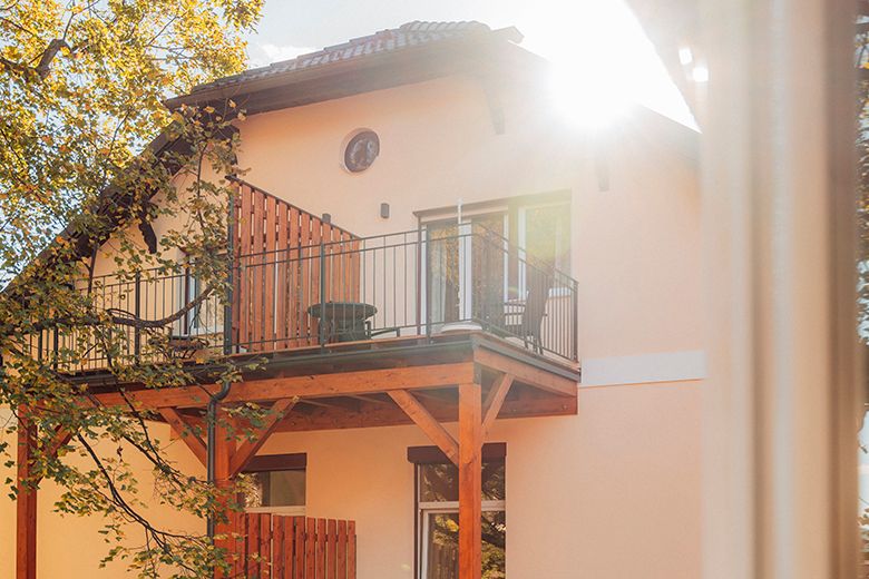 Haus mit Balkon und Sonnenschein durch Bäume.