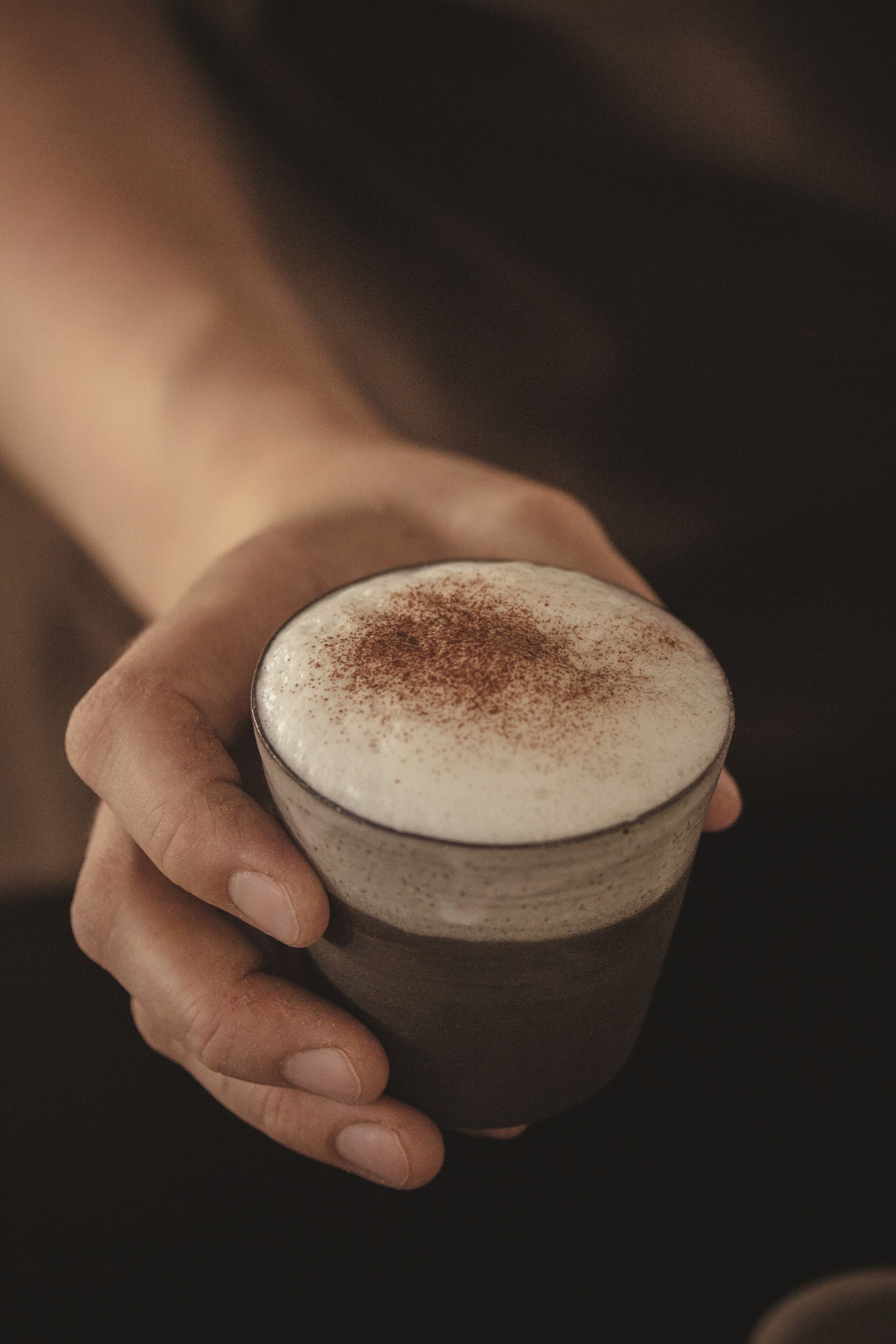 Nahaufnahme einer Hand, die ein Glas mit Cappuccino und Milchschaum hält.