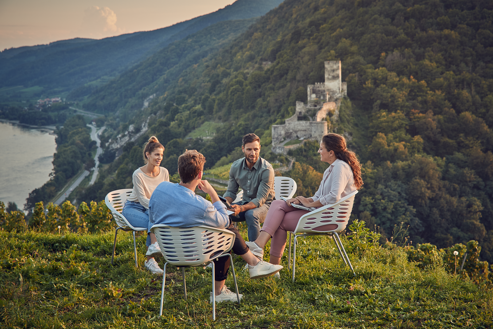 Inmitten der sanften Hügel und der atemberaubenden Landschaft versammeln sich Freunde, um die Schönheit der Natur zu genießen. Die warmen Sonnenstrahlen tauchen die Szene in ein goldenes Licht, während der Blick auf die majestätischen Ruinen im Hintergrund die Fantasie anregt. Hier wird der Sommer in den Bergen zu einem unvergesslichen Erlebnis.