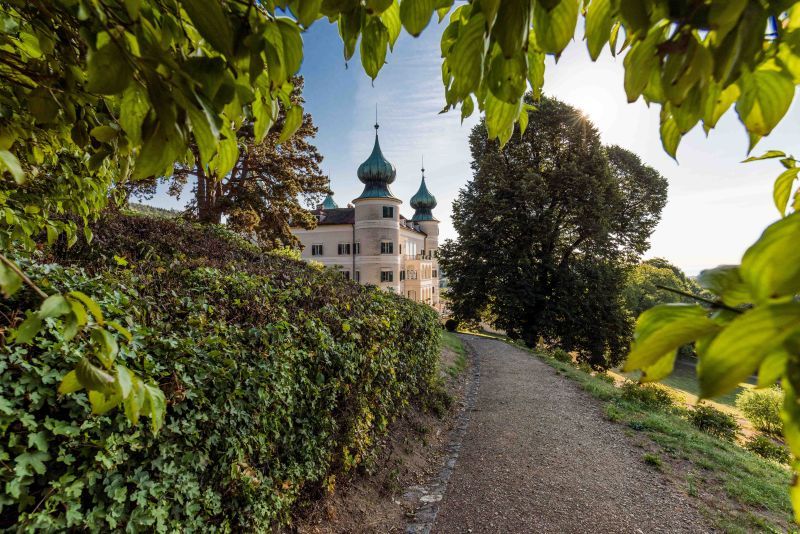 Schloss Artstetten mit grünen Zwiebeltürmen, umgeben von Bäumen und einem Weg im Vordergrund.