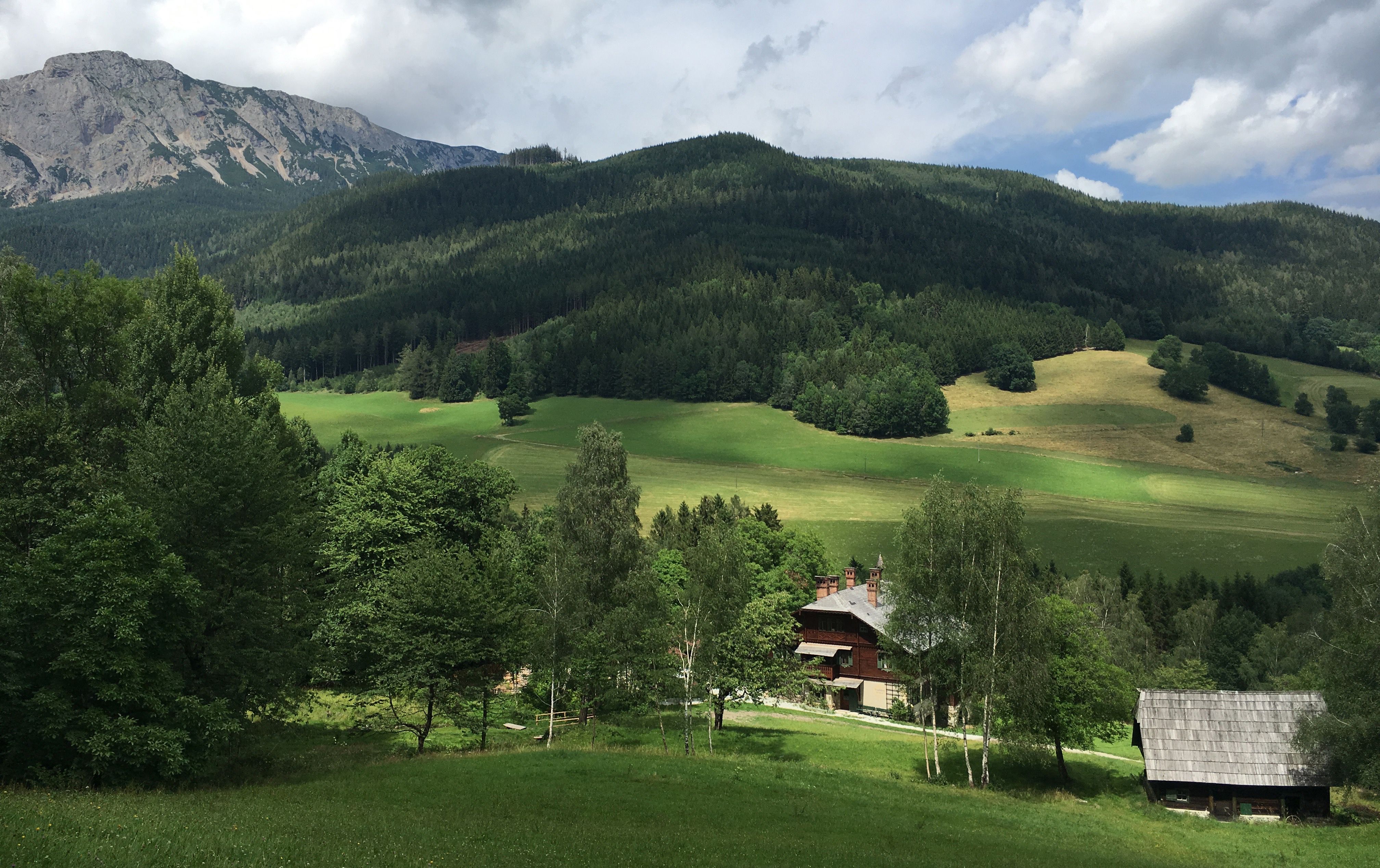 Ein Bauernhof in einer grünen, hügeligen Landschaft mit Bergen im Hintergrund.