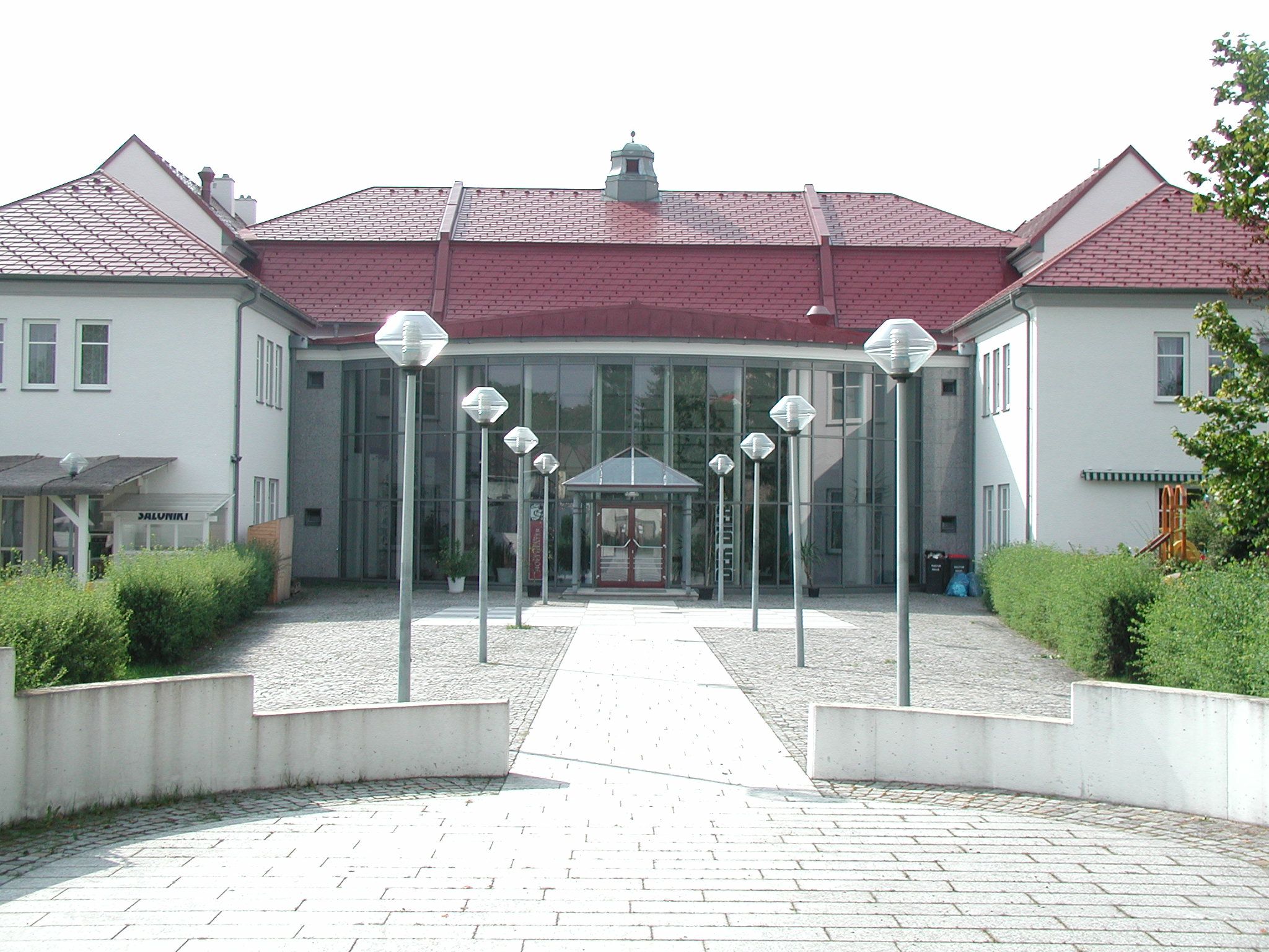 Eingang eines modernen Kulturhauses mit Glasfassade und roten Dächern.