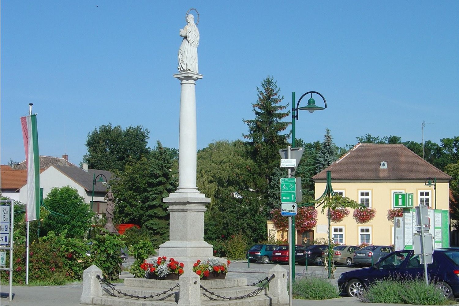 Statue auf einer Säule in einem Platz in Haugsdorf, umgeben von Gebäuden und Bäumen.