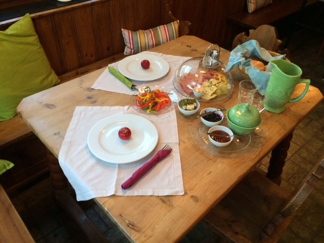 Ein gedeckter Frühstückstisch mit Tellern, Besteck, Aufschnitt, Gemüse und Getränken.