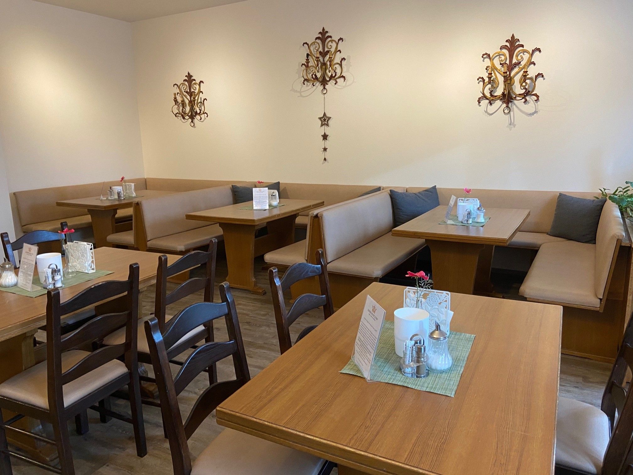 Gemütlicher Frühstücksbereich mit Holztischen und gepolsterten Sitzbänken, dekoriert mit Wandornamenten.