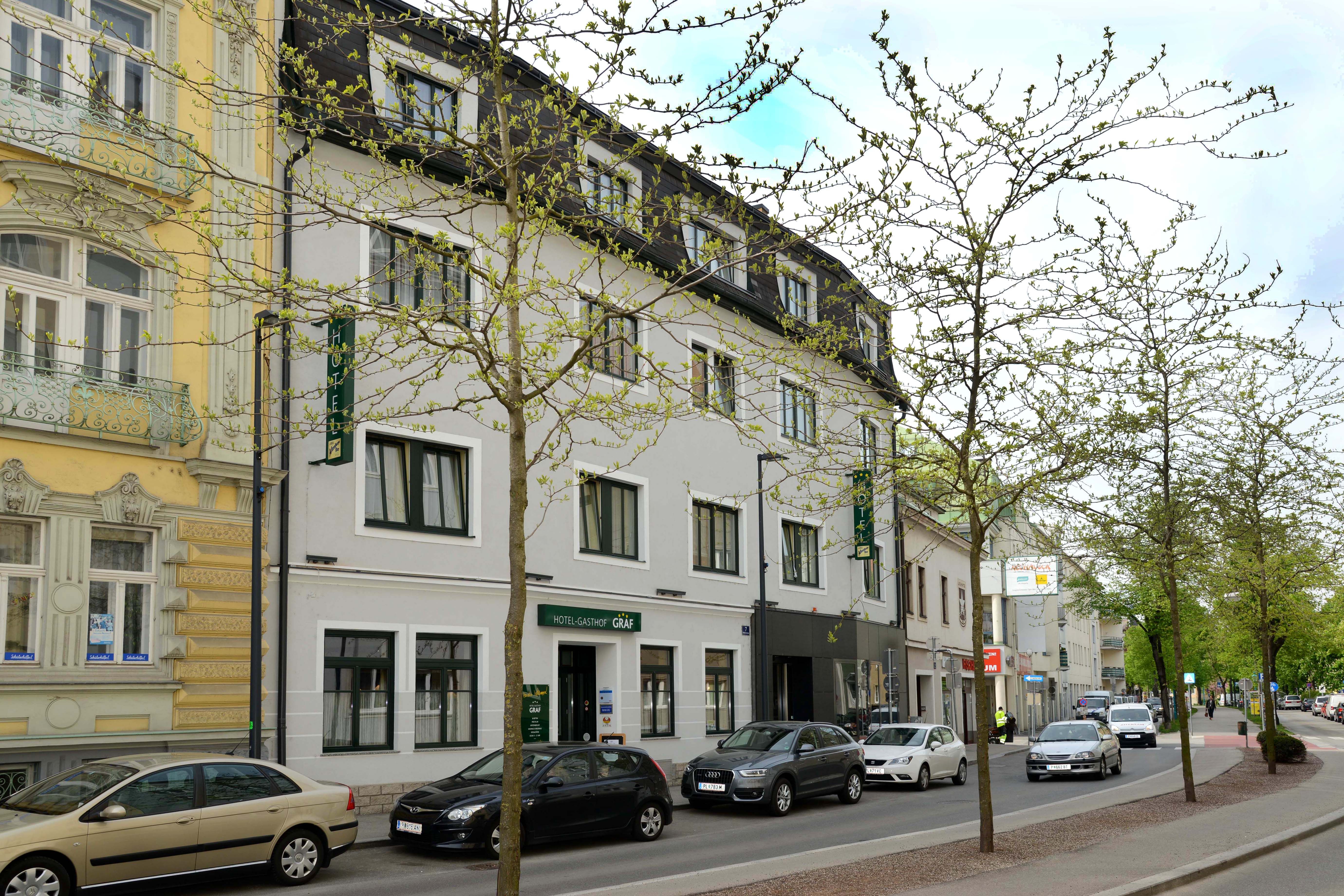 Straßenansicht des Hotel-Gasthof Graf mit parkenden Autos und Bäumen.