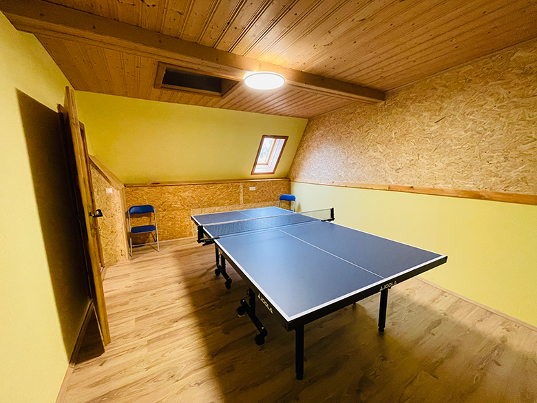 Ein Spielzimmer mit Tischtennisplatte, gelben Wänden und Holzdecke.