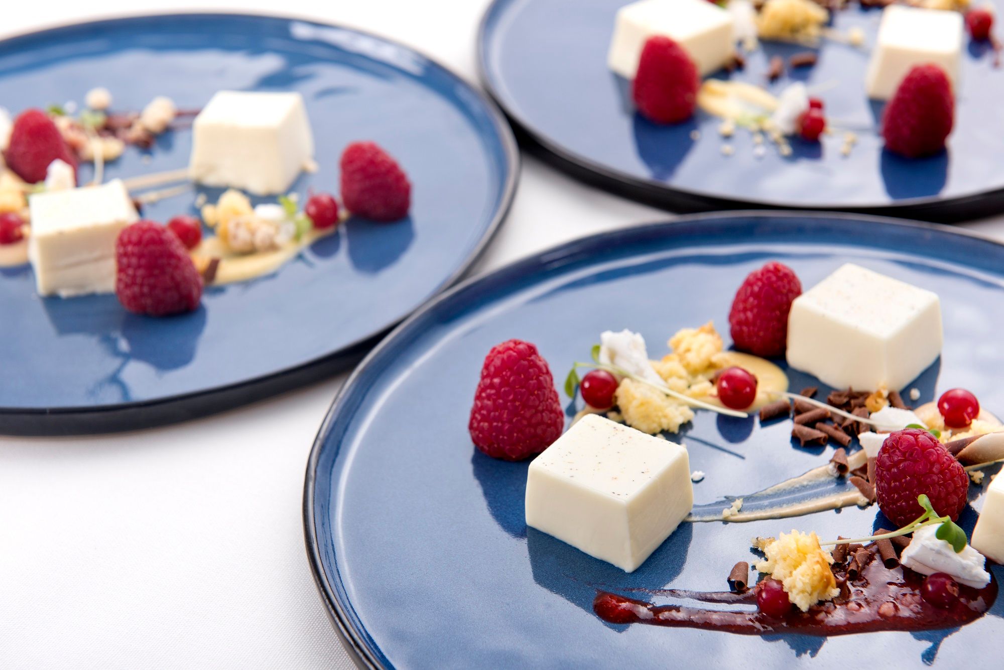 Elegante Dessertpräsentation auf blauen Tellern mit Himbeeren, Creme und Schokoladensplittern.