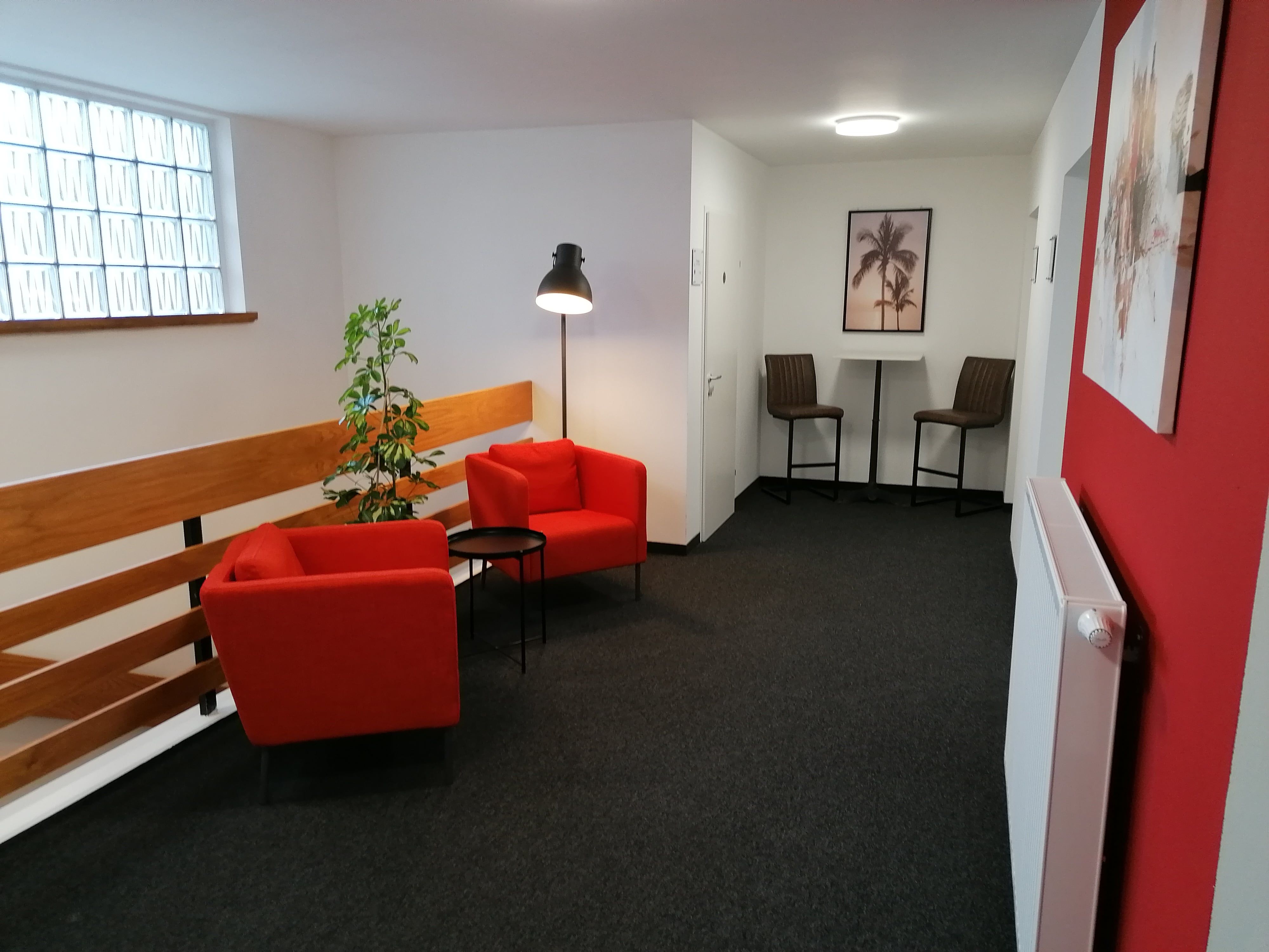 Gemütliche Sitzecke mit roten Sesseln und Stehlampe in einem Flur.