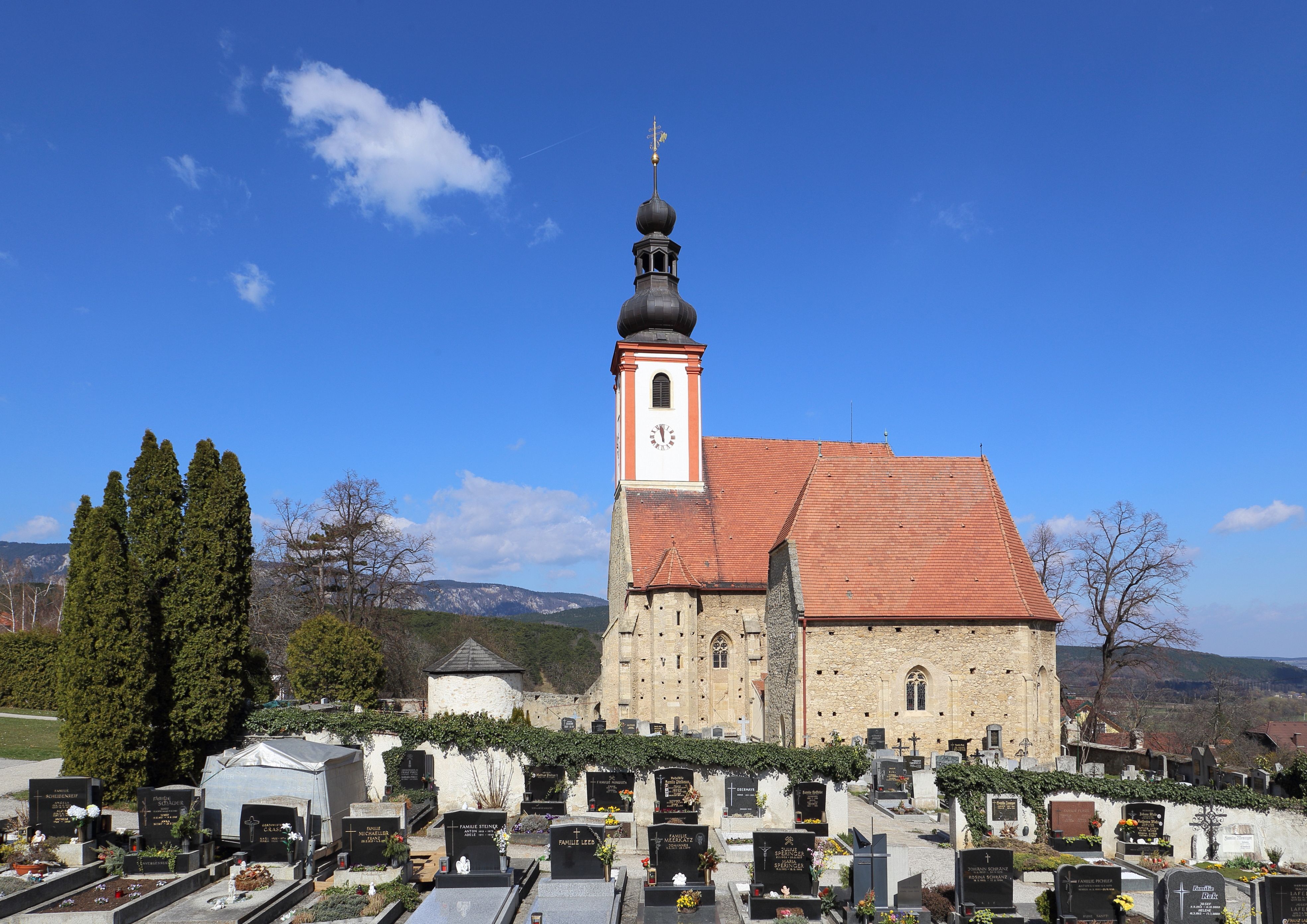 Kirche mit Friedhof im Vordergrund und blauem Himmel.