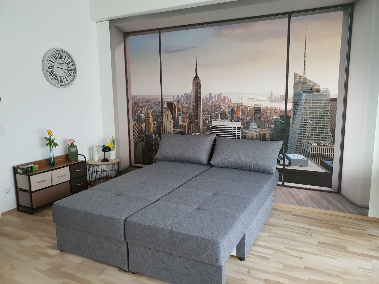 Zimmer mit grauem Sofa und Fototapete von New York Skyline.