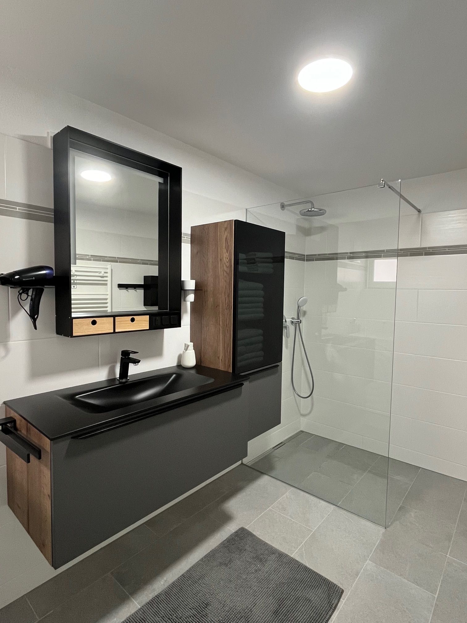 Modernes Badezimmer mit schwarzem Waschbecken, Spiegel, Regendusche und grauen Fliesen.