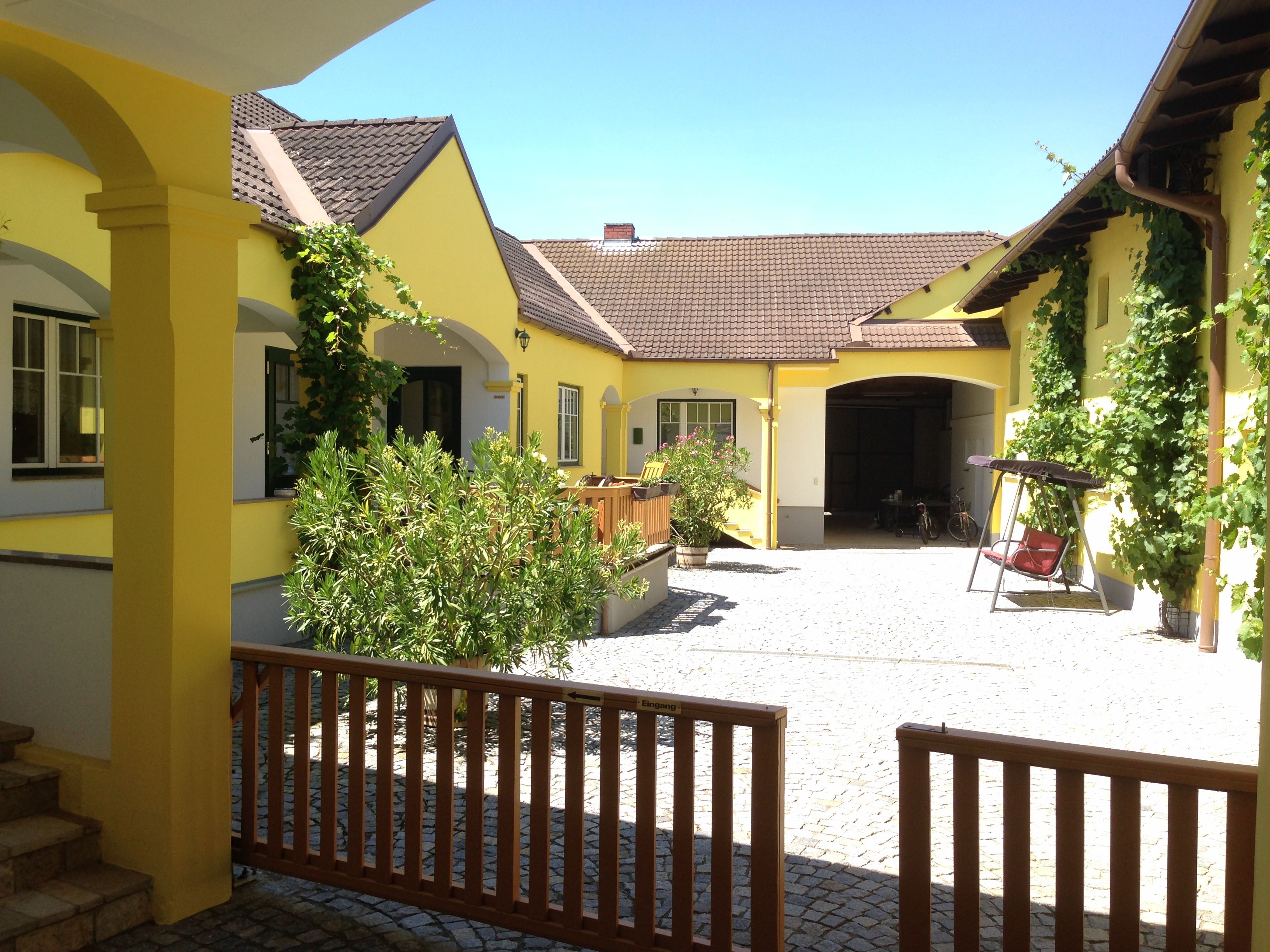 Innenhof eines gelben Winzerhofs mit Pflanzen und Schaukel.