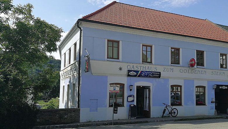 Ein zweistöckiges Gebäude mit der Aufschrift 'Gasthaus zum Goldenen Stern' und einem Fahrrad davor.